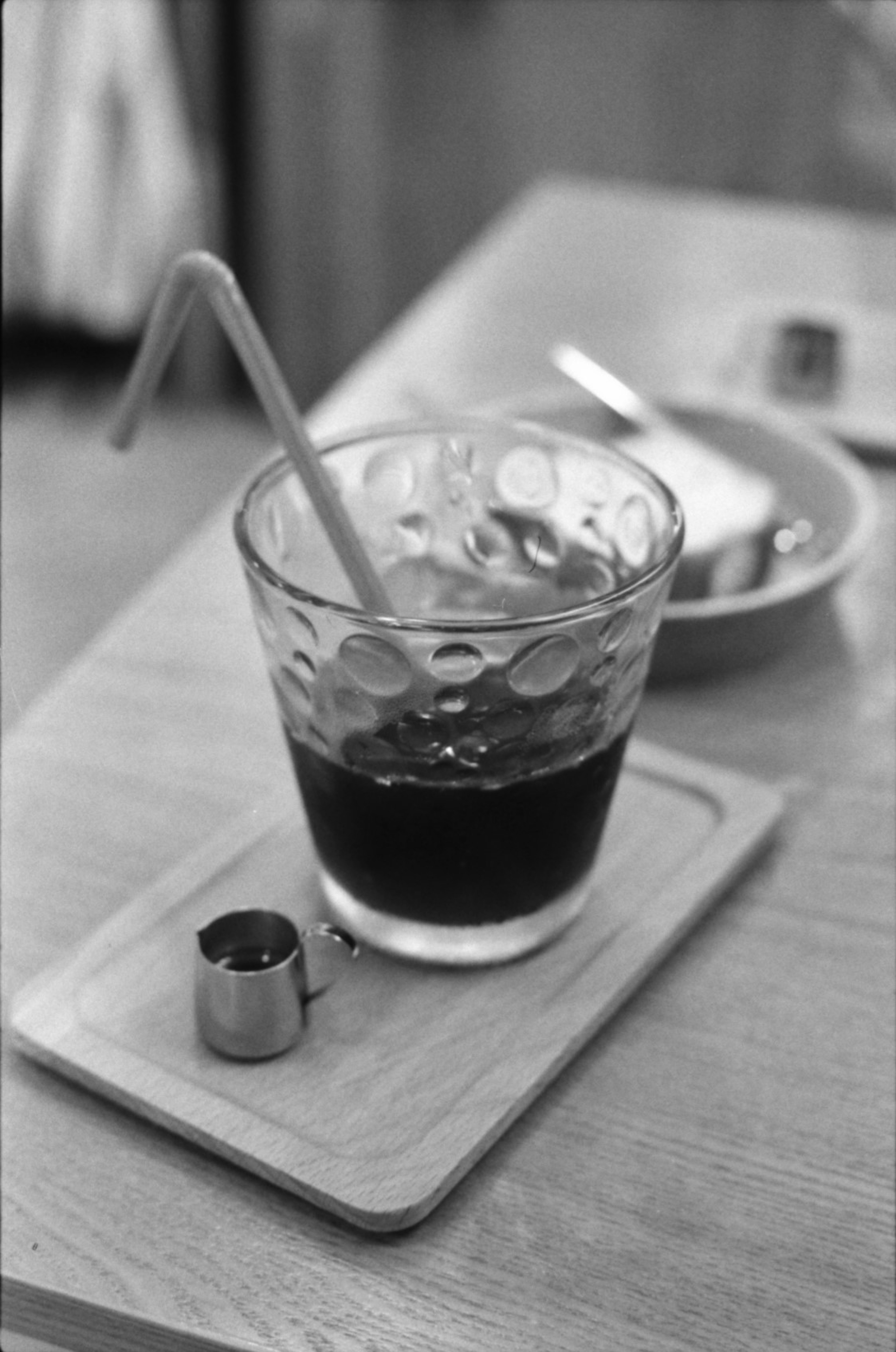 A clear glass of iced coffee with a straw on a wooden tray