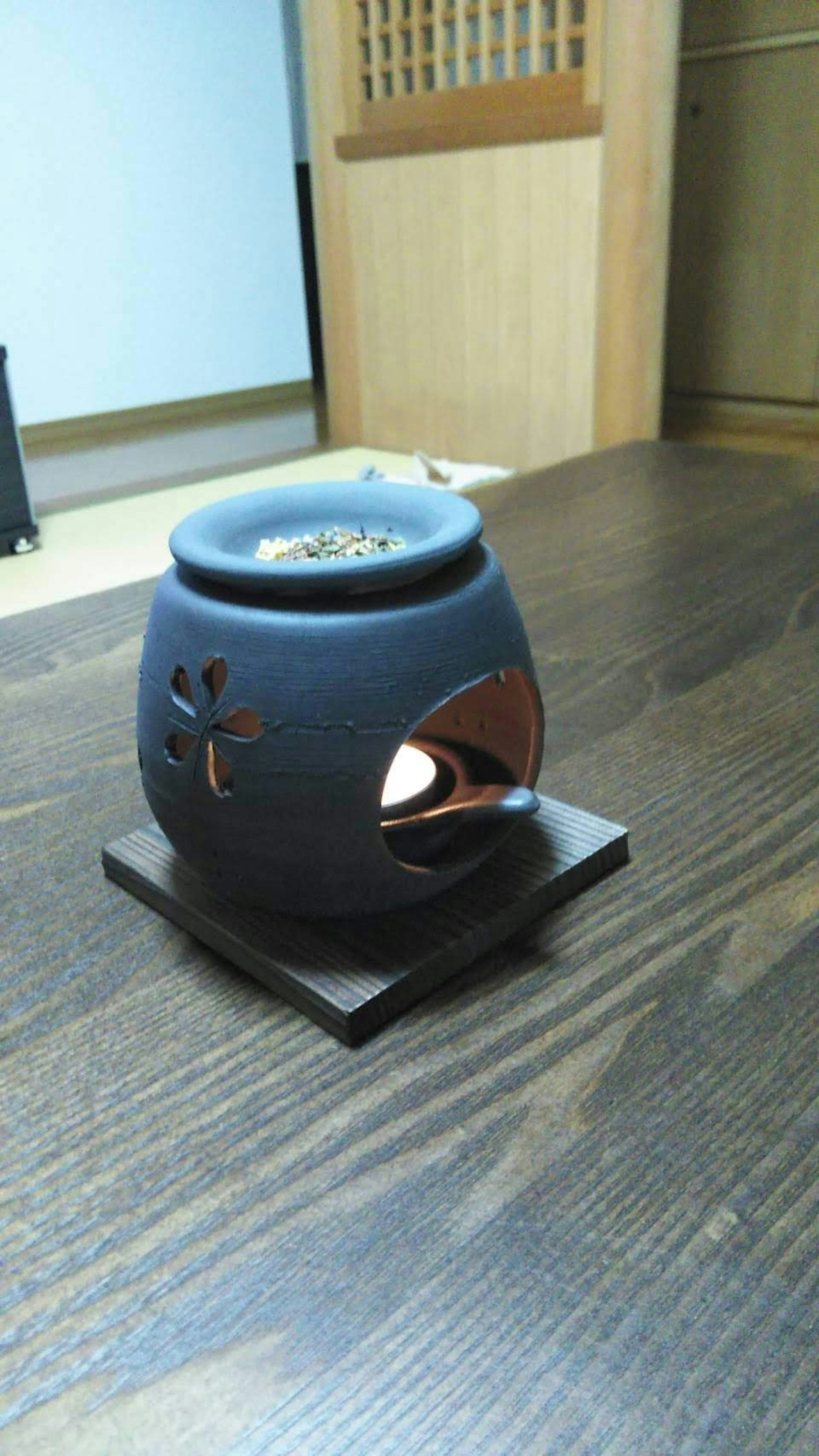 Un pot à aromathérapie en céramique noire sur une table en bois avec une bougie allumée à l'intérieur