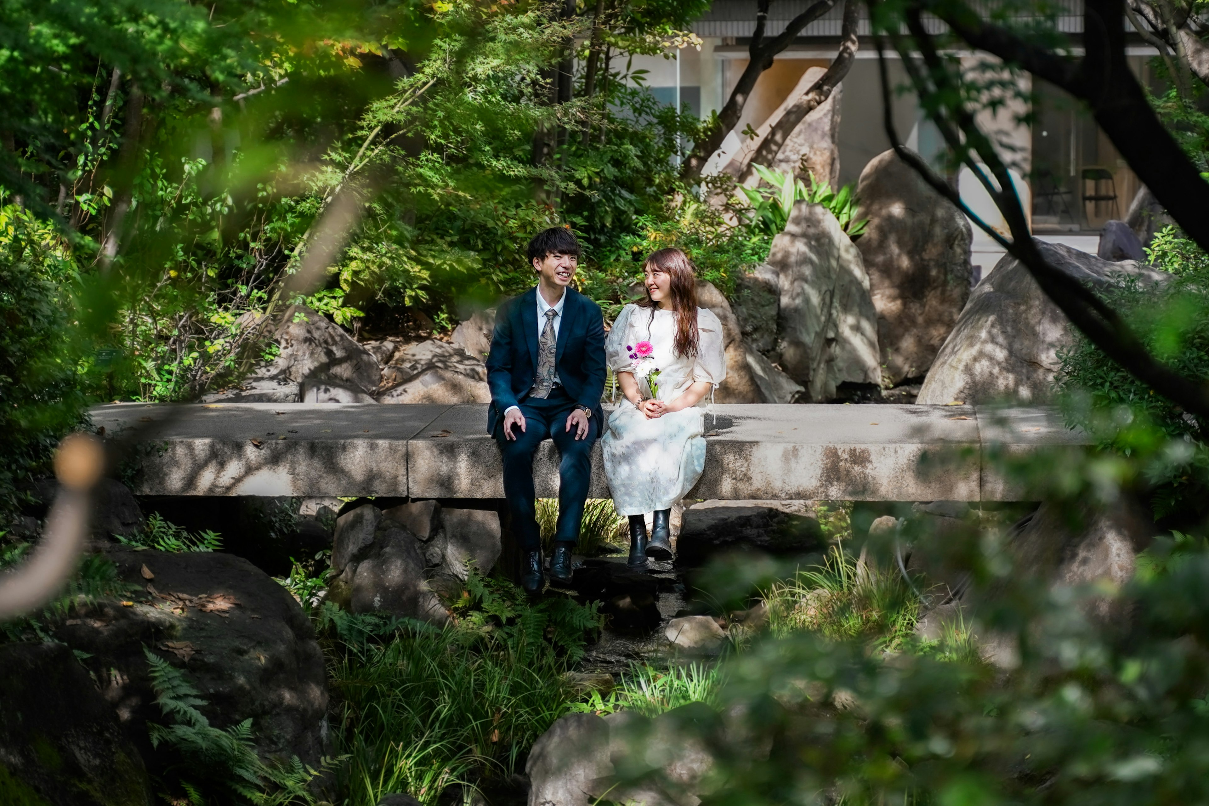 Novio y novia sentados en un puente en un jardín rodeado de vegetación