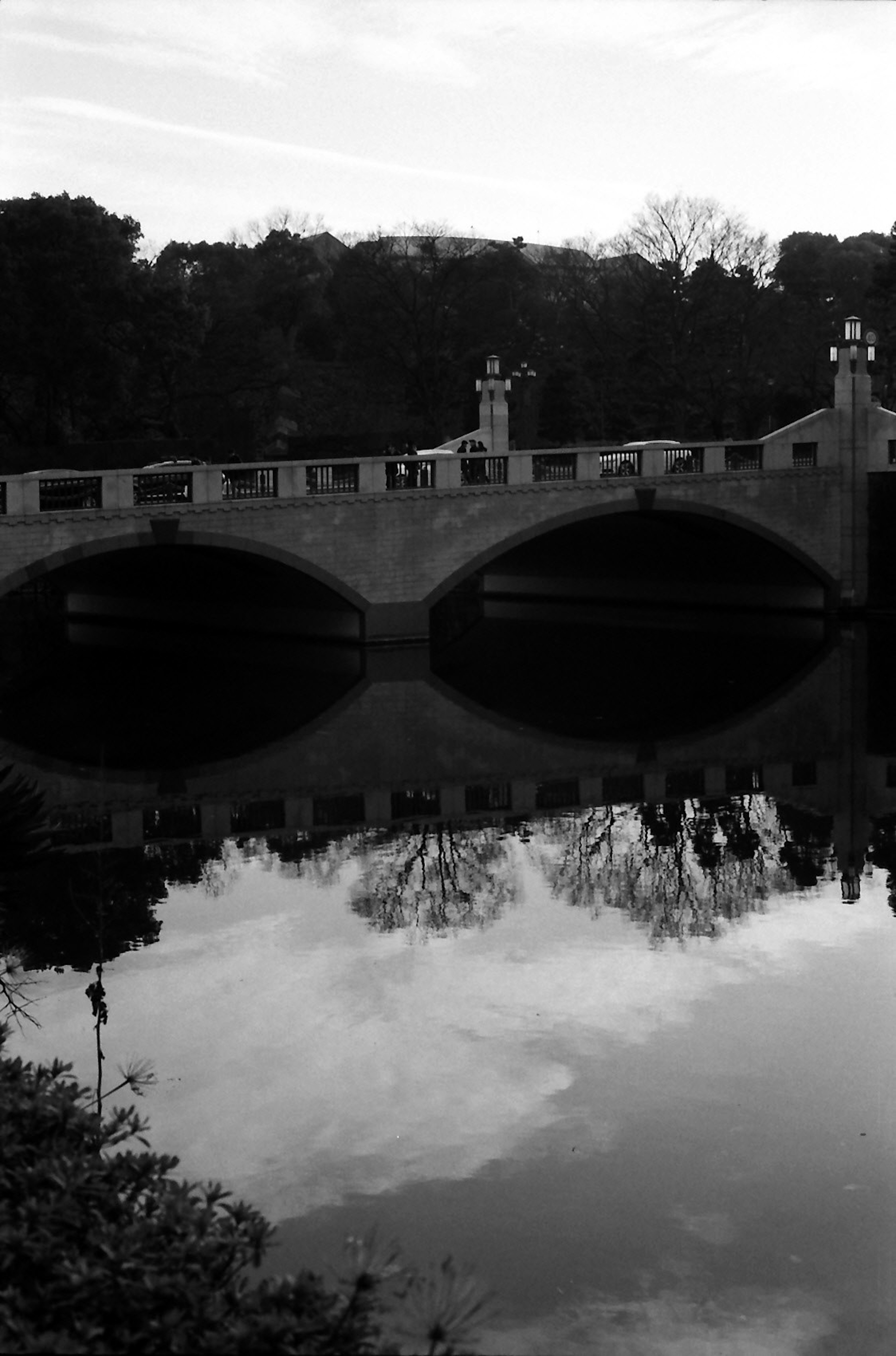 Image en noir et blanc d'un pont avec des reflets sur une eau calme