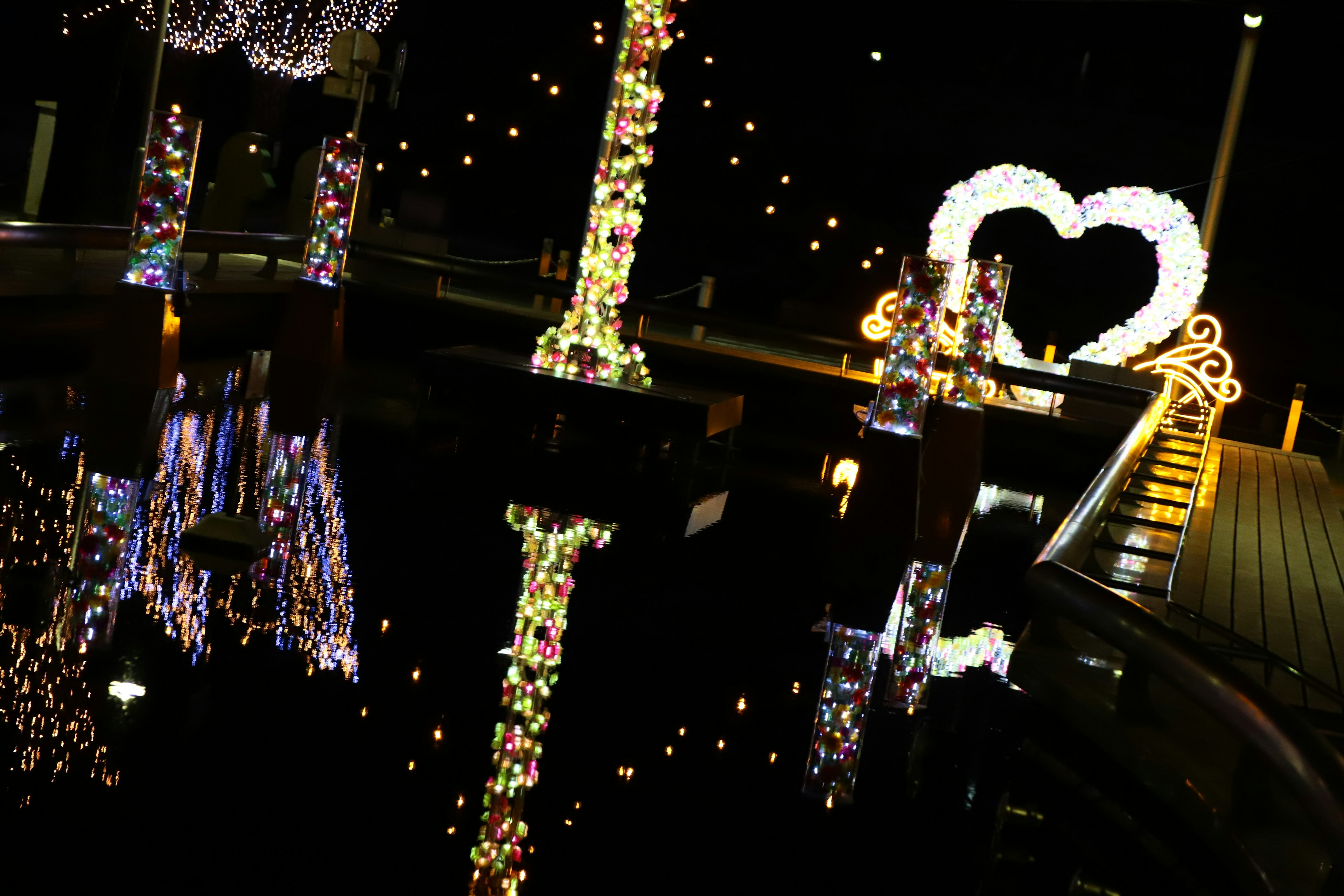 Colorful light decorations and heart shape reflected in a night pond