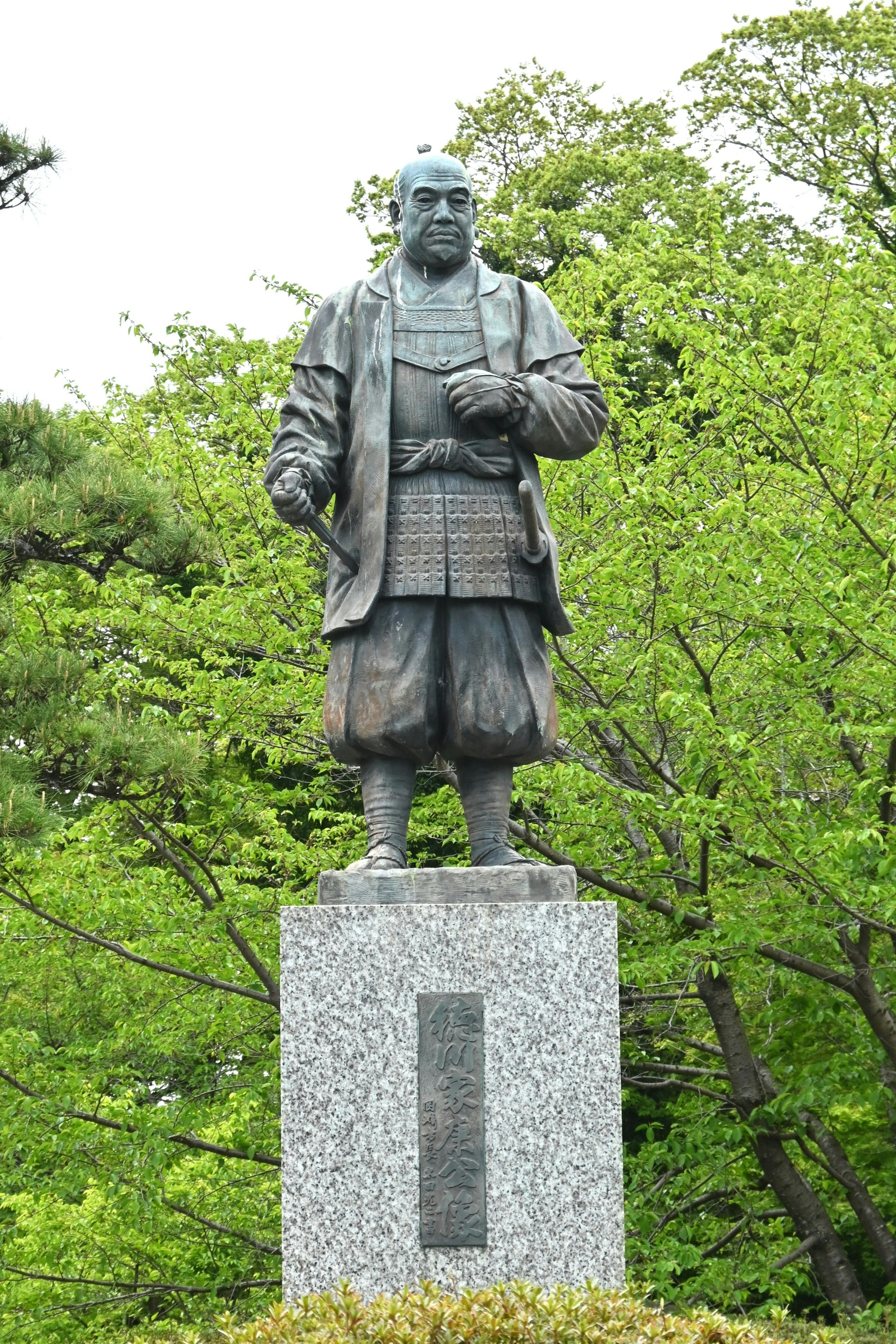 Bronze statue of a samurai standing with a green background