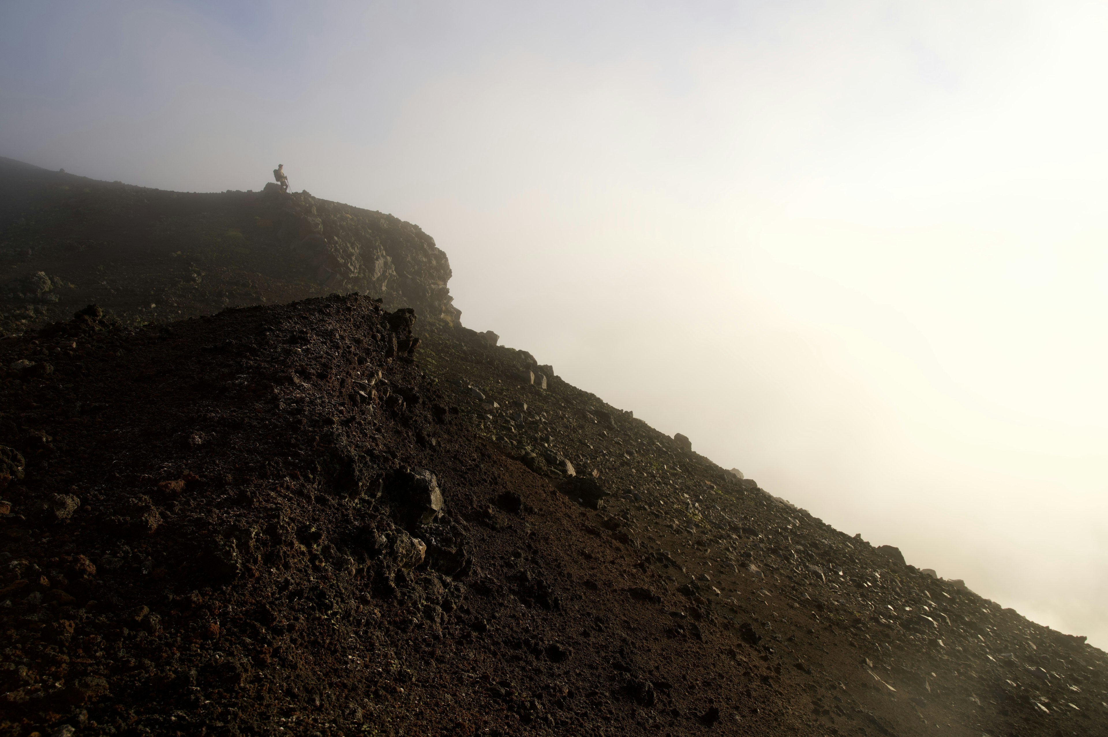 Mountain slope shrouded in fog with a small figure