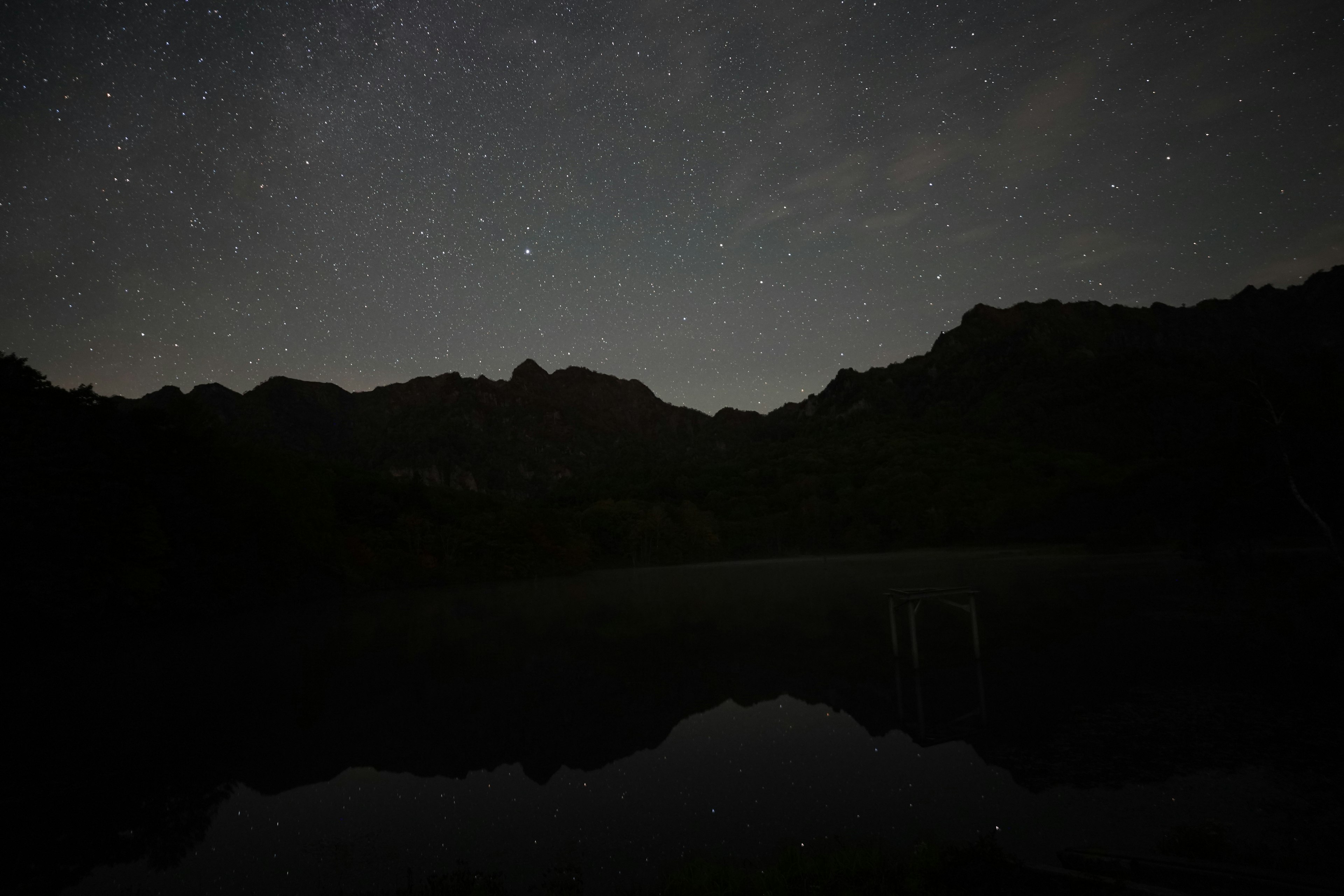 Silueta de montañas y un lago tranquilo bajo un cielo estrellado