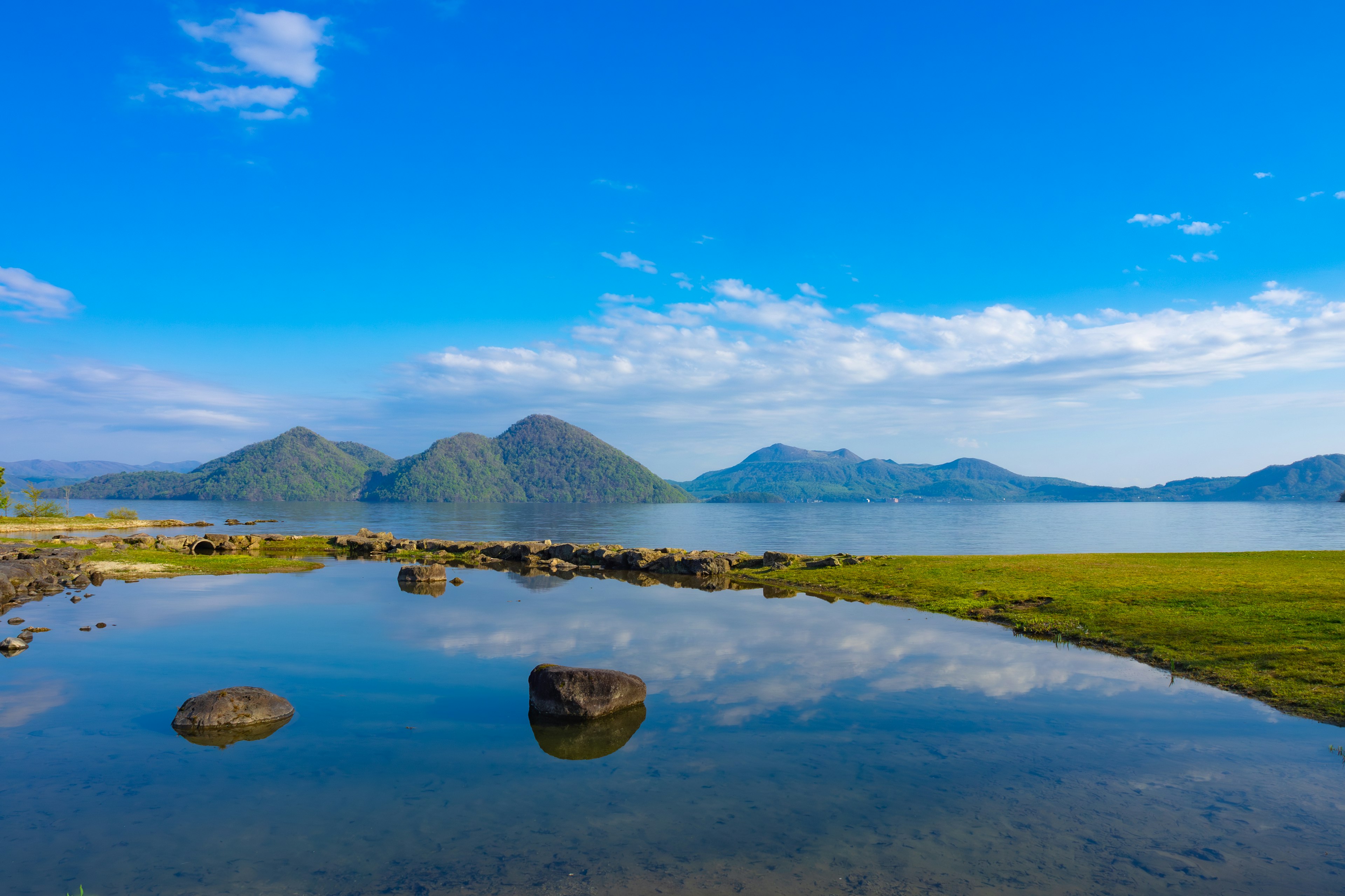 青空と山々の美しい風景 反射する水面と緑の草地