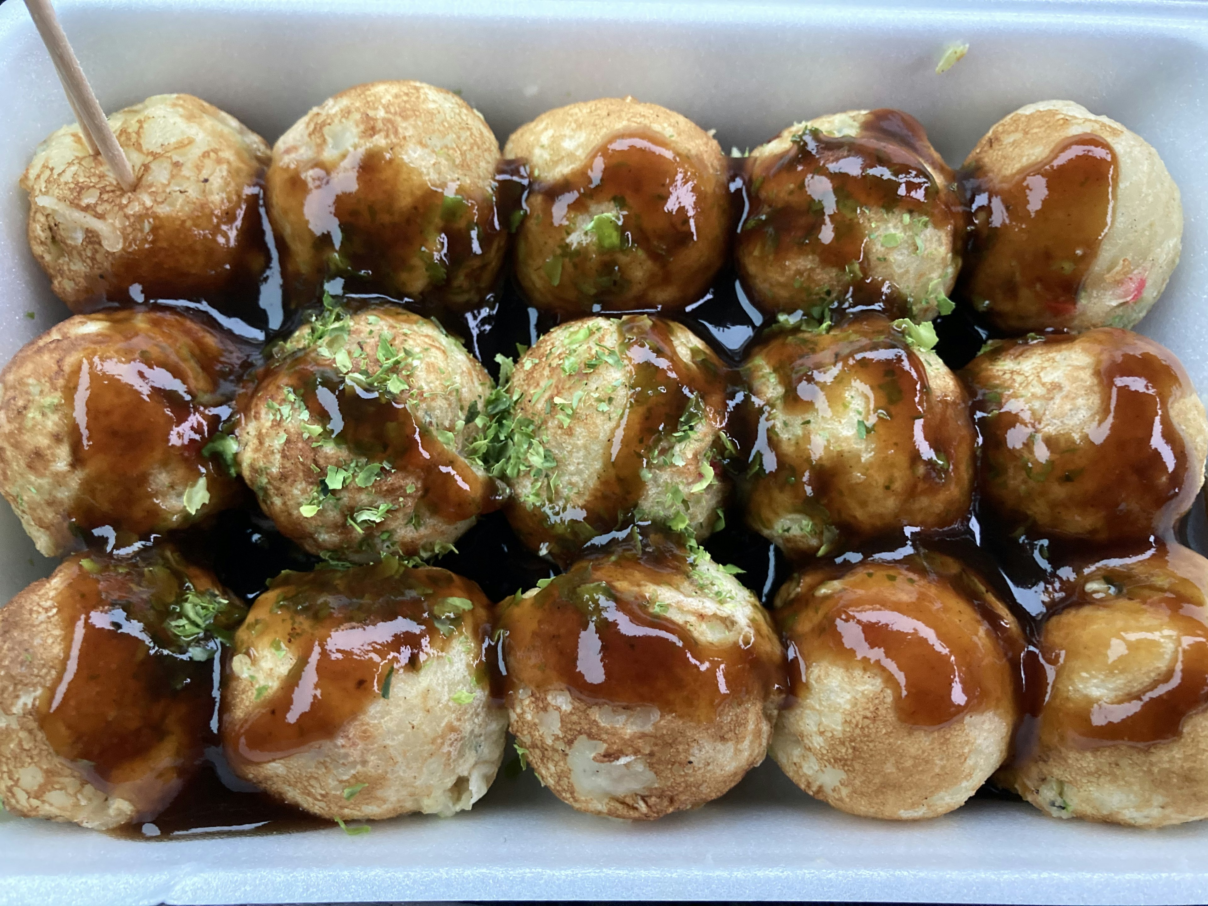 Eine Portion Takoyaki mit Sauce und grünen Algen garniert