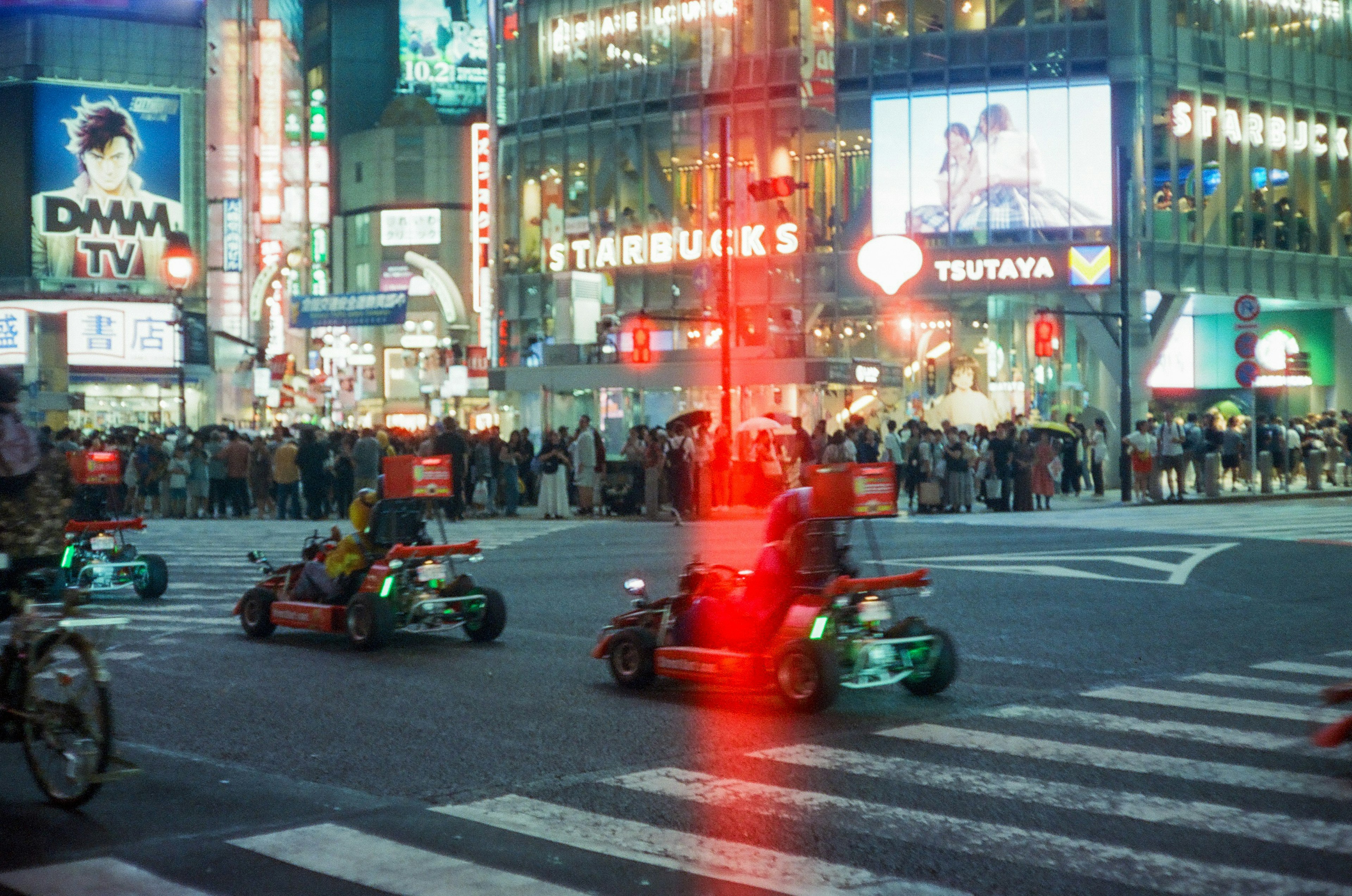 Cảnh đêm tại giao lộ Shibuya với xe go-kart và đám đông