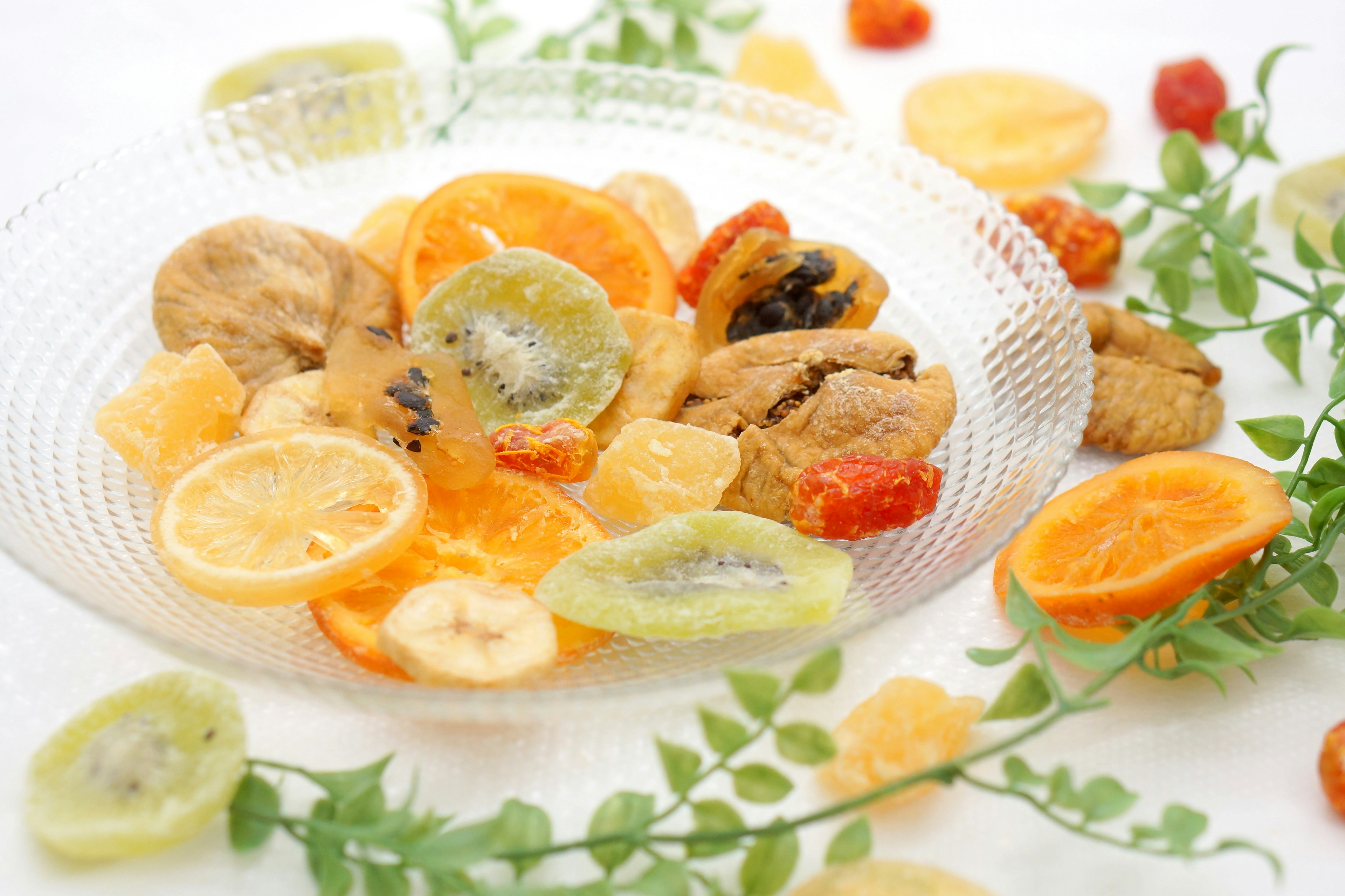 Frutas secas coloridas y galletas dispuestas en un plato de vidrio con hojas verdes