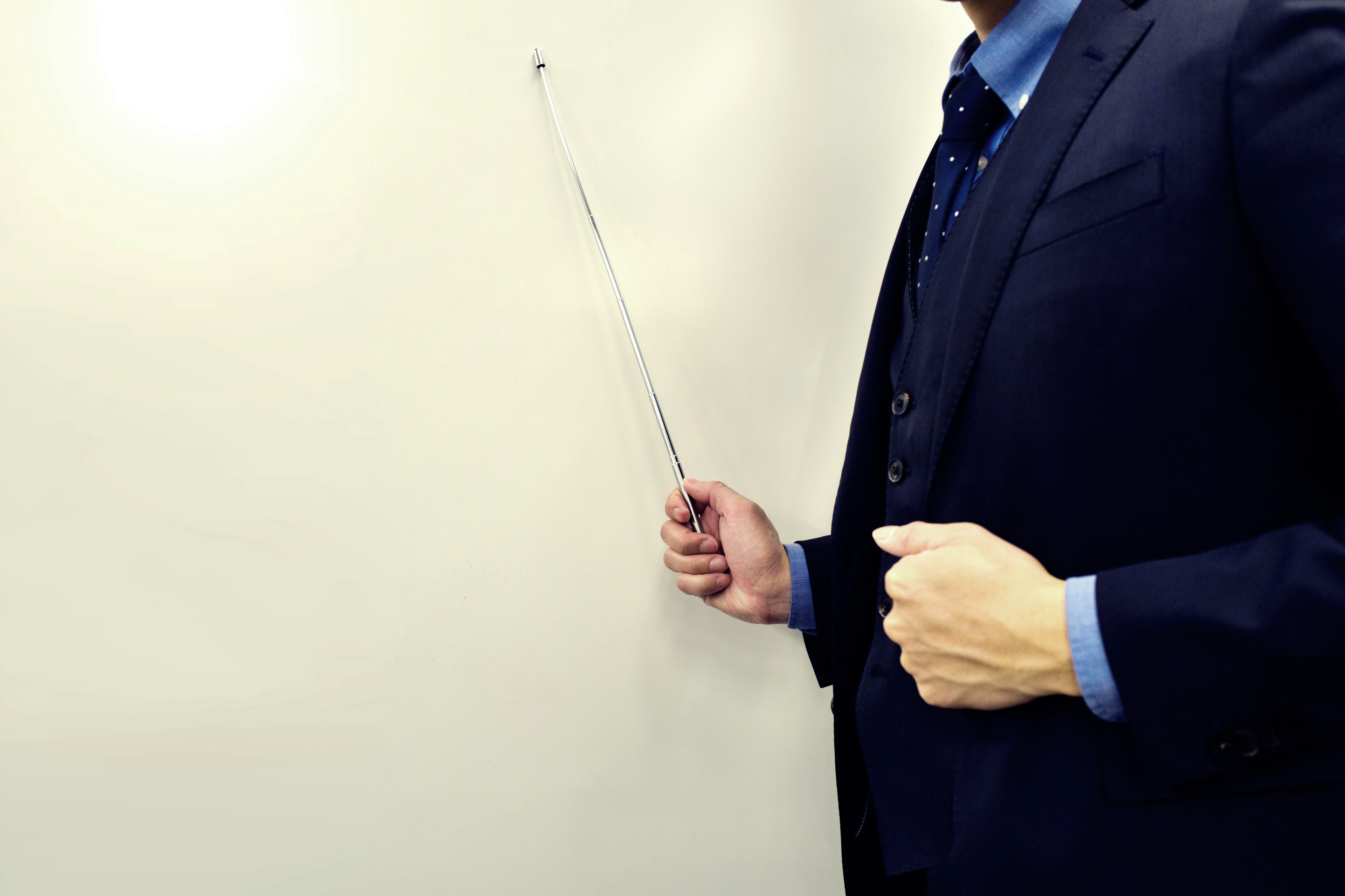 A man in a suit holding a pointer near a whiteboard