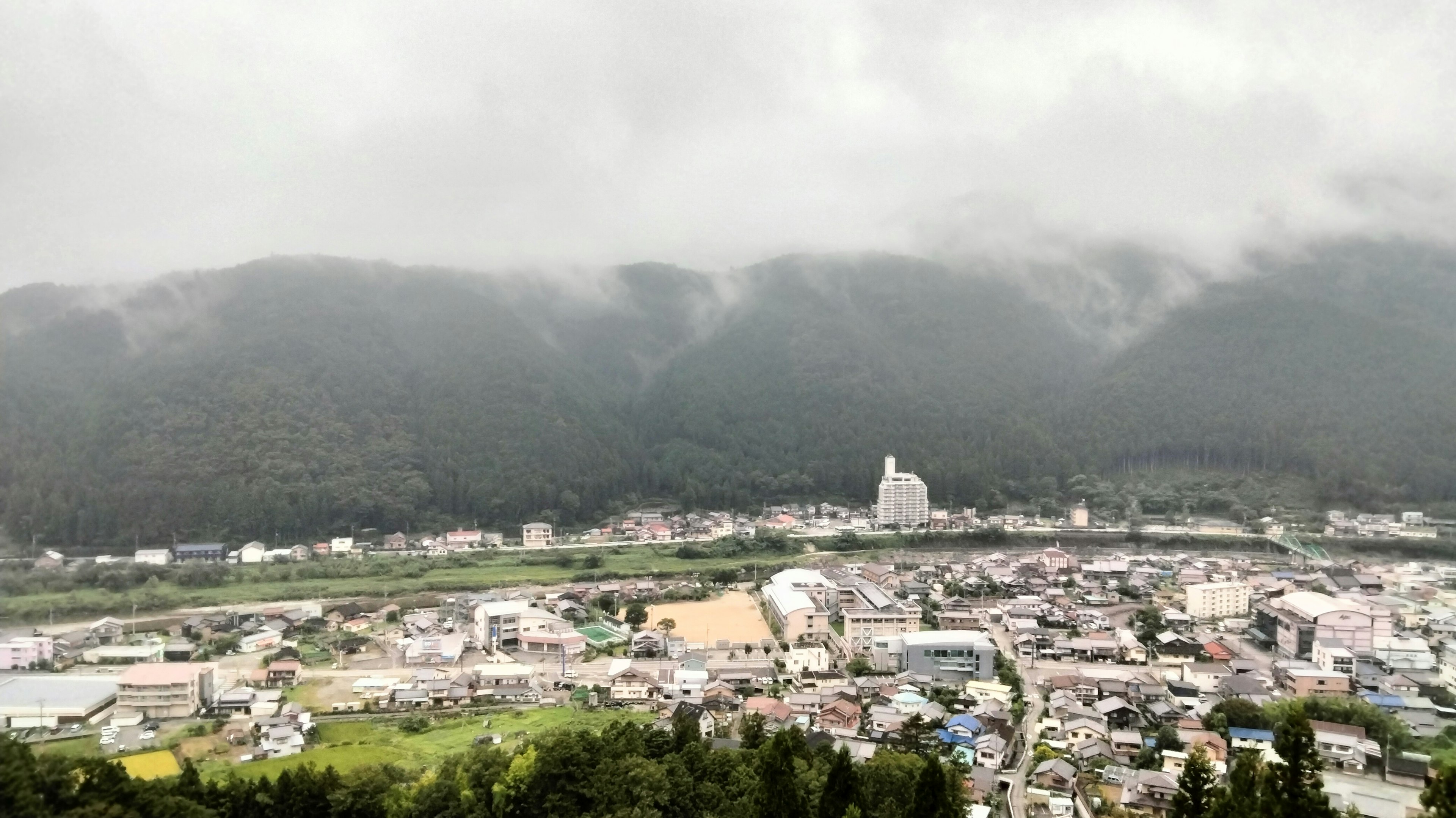 A serene town landscape surrounded by mountains with a foggy sky and lush greenery