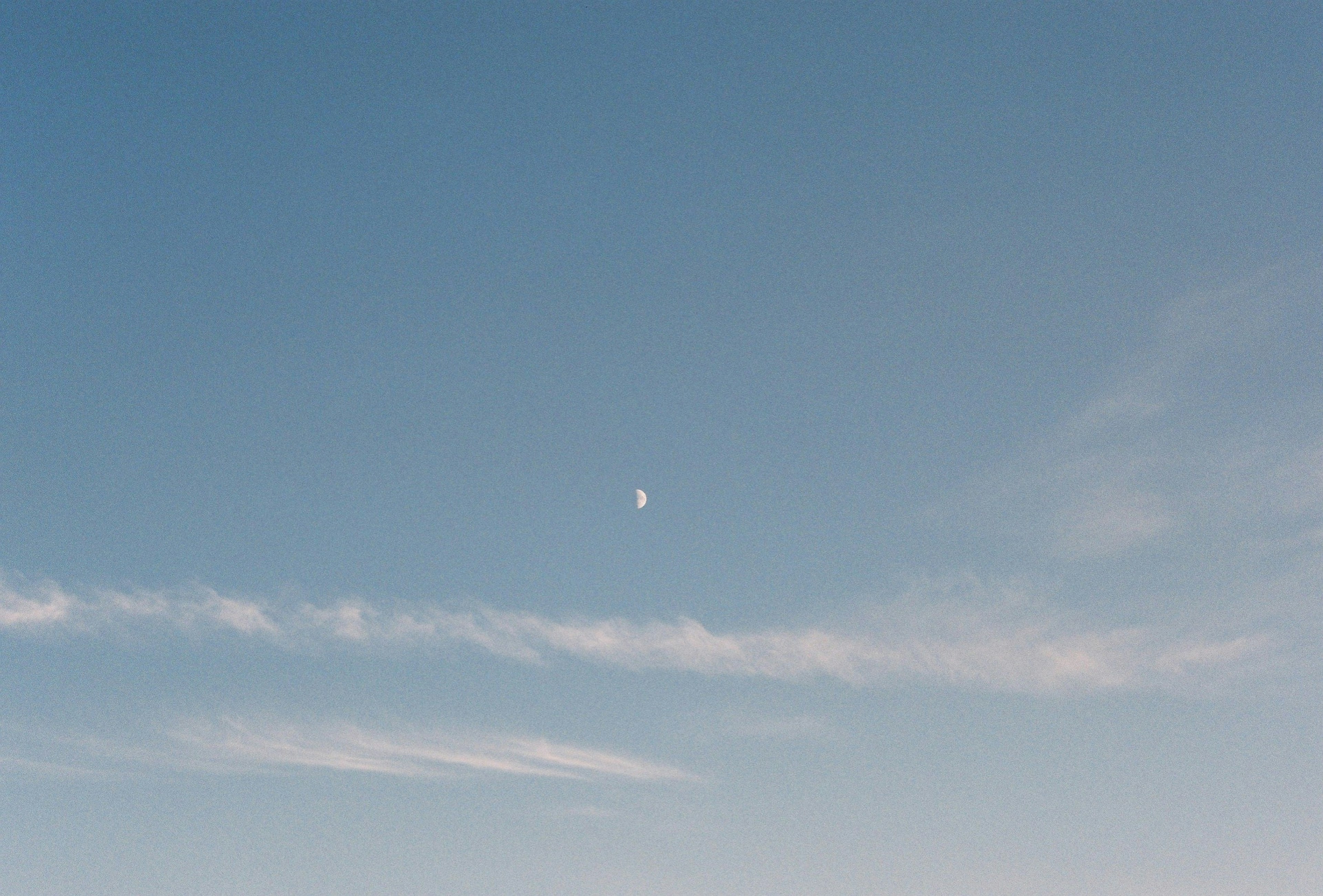 Un ciel bleu clair avec une lune croissante et des nuages légers