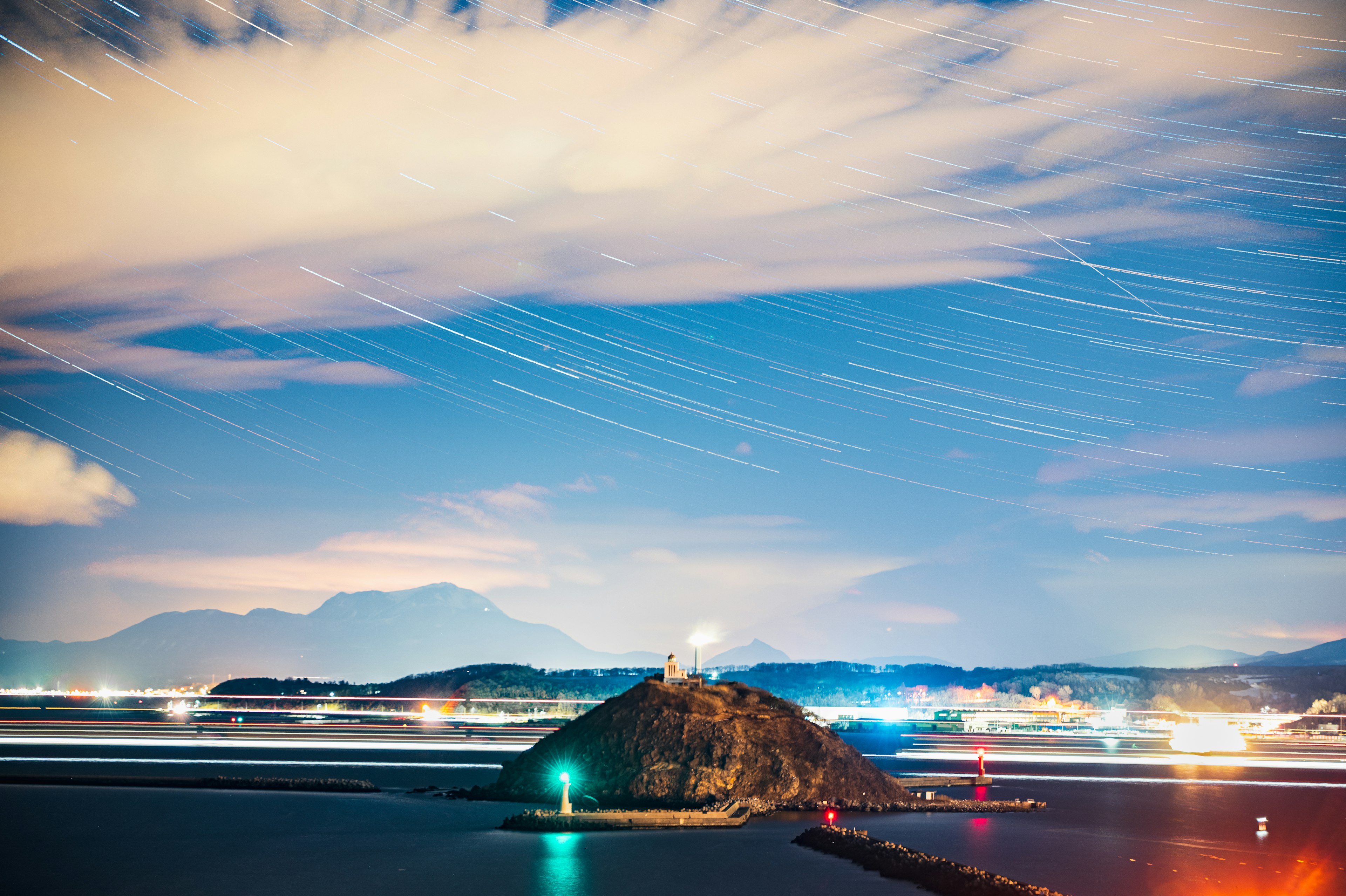 夜空中星轨在海岸景观和灯塔上方