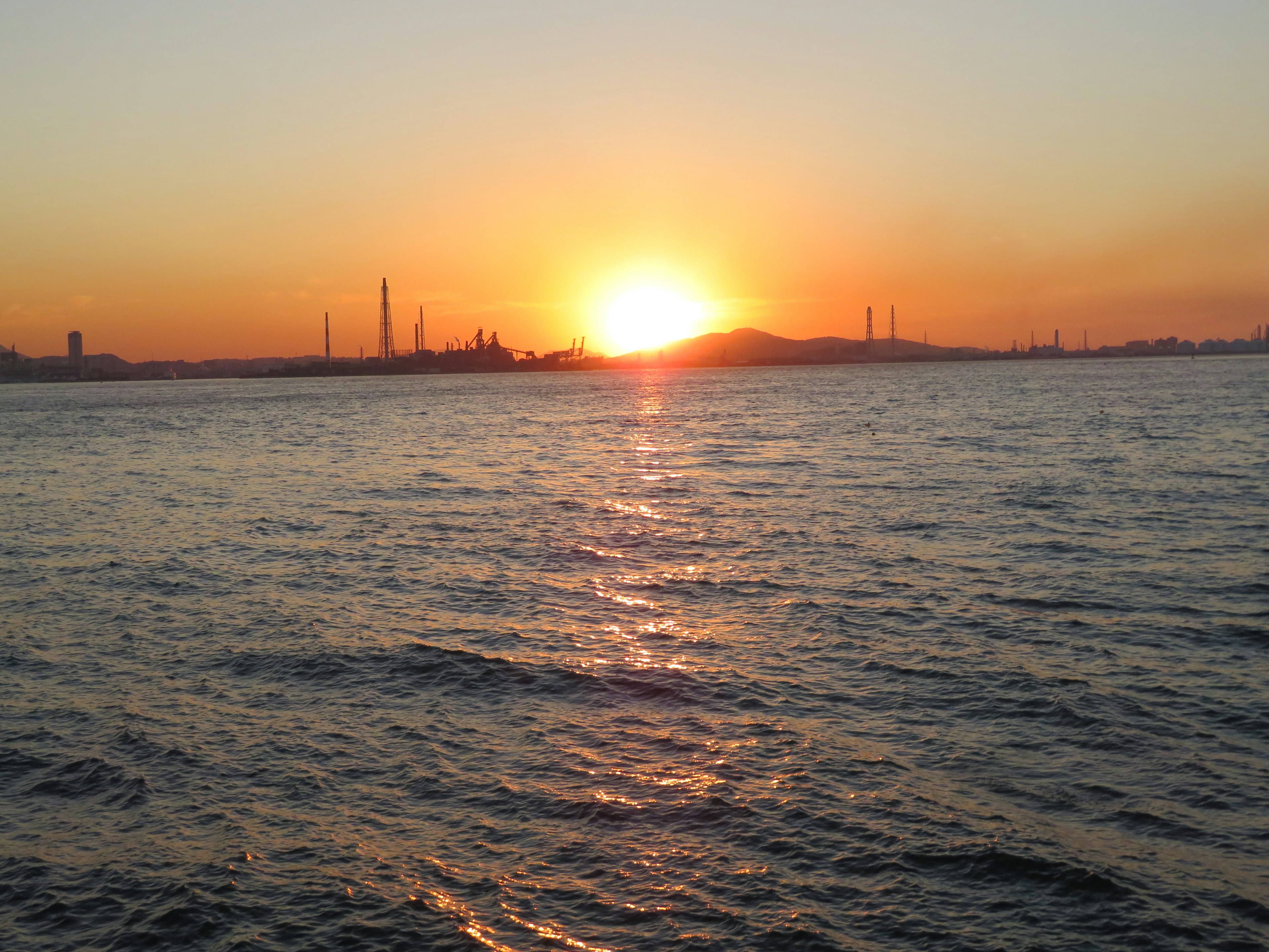 Atardecer sobre el mar con siluetas de fábricas