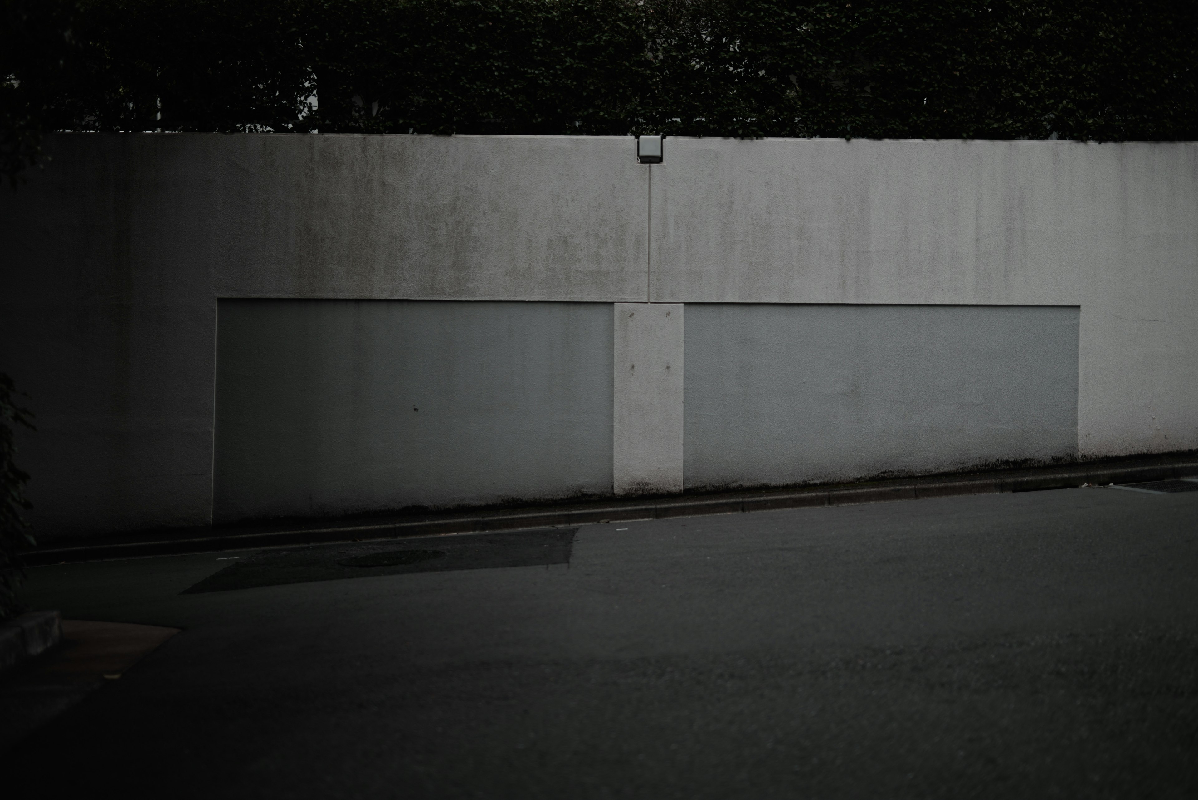 Concrete wall with two garage doors and paved road