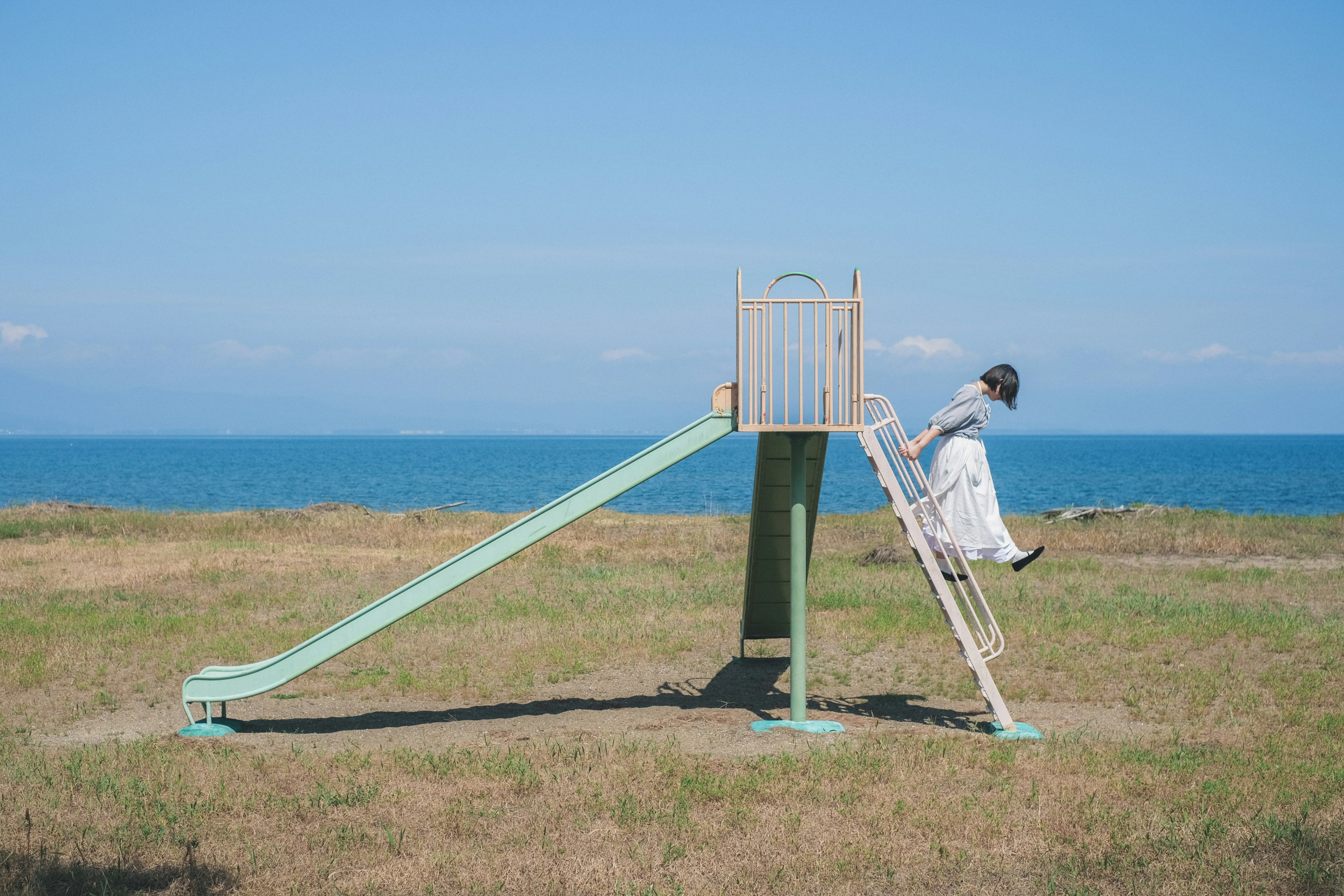 Una donna in abito bianco scivola giù da uno scivolo verde con un oceano blu sullo sfondo