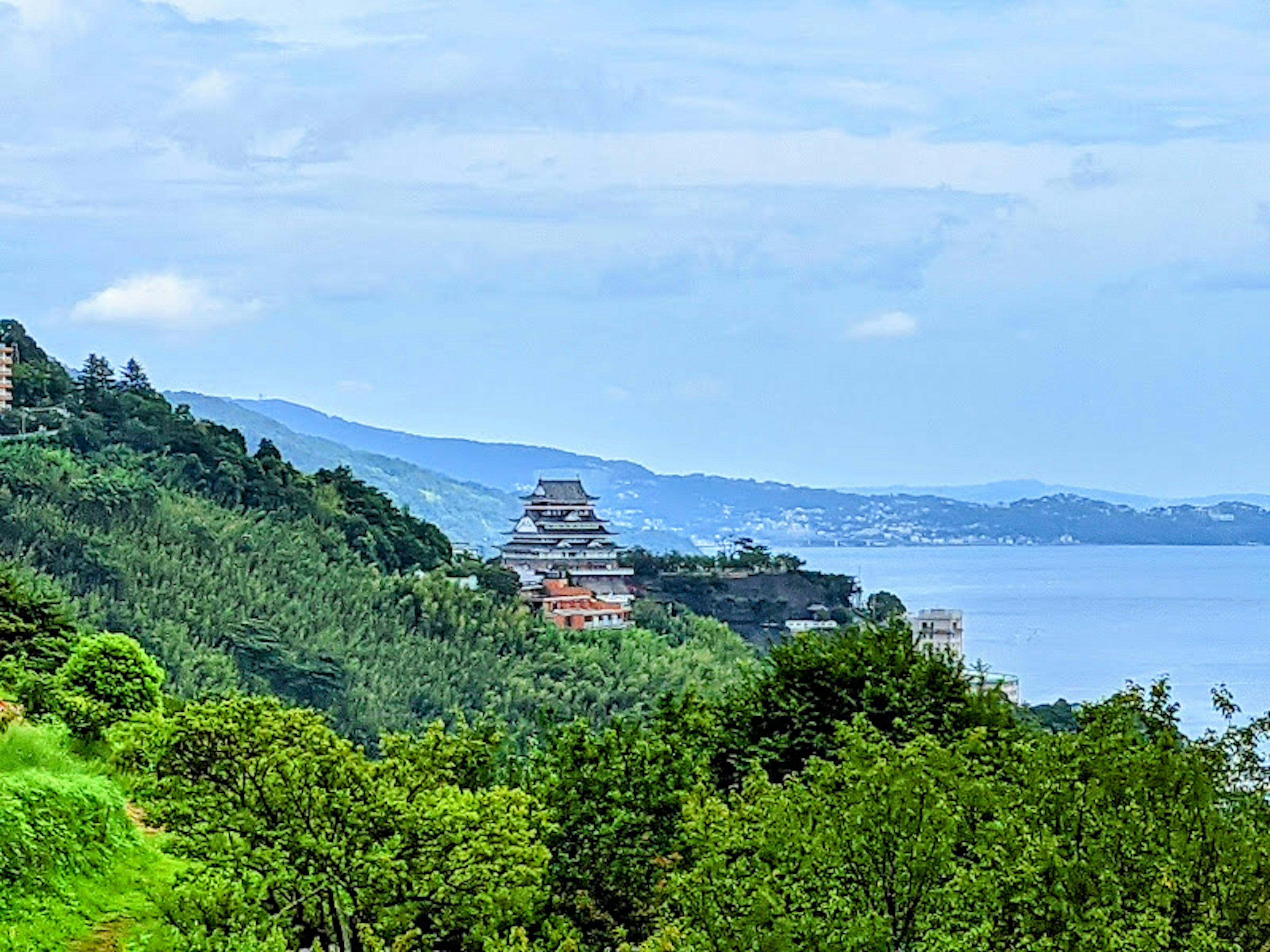 Temple surrounded by lush green hills with a blue sky and ocean in the background