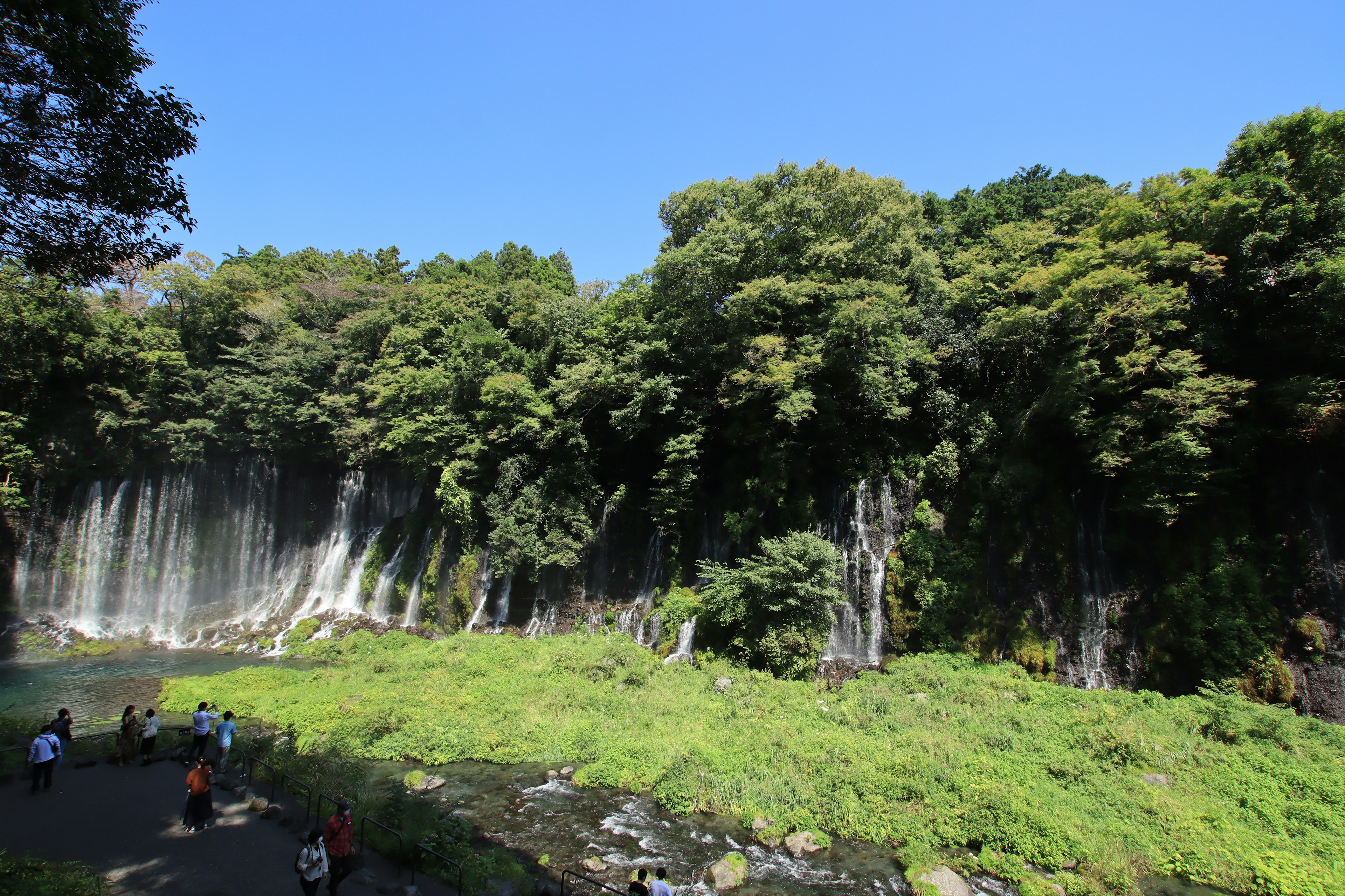 Wasserfall umgeben von üppigem Grün und Besuchern, die die Aussicht genießen