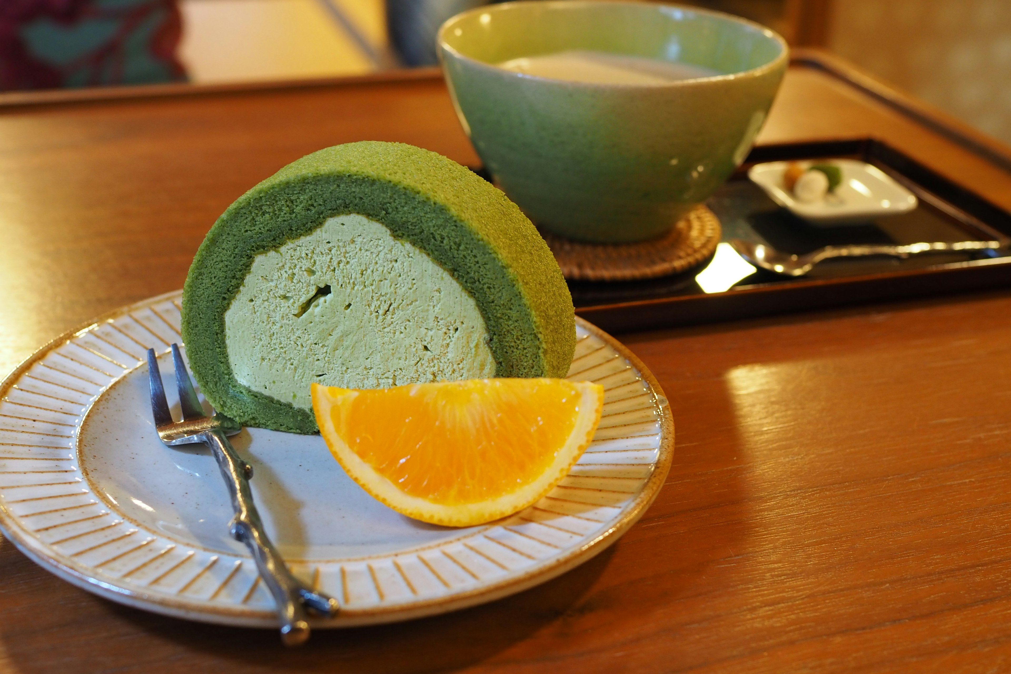 Pastel enrollado verde servido con una rodaja de naranja en un plato decorativo