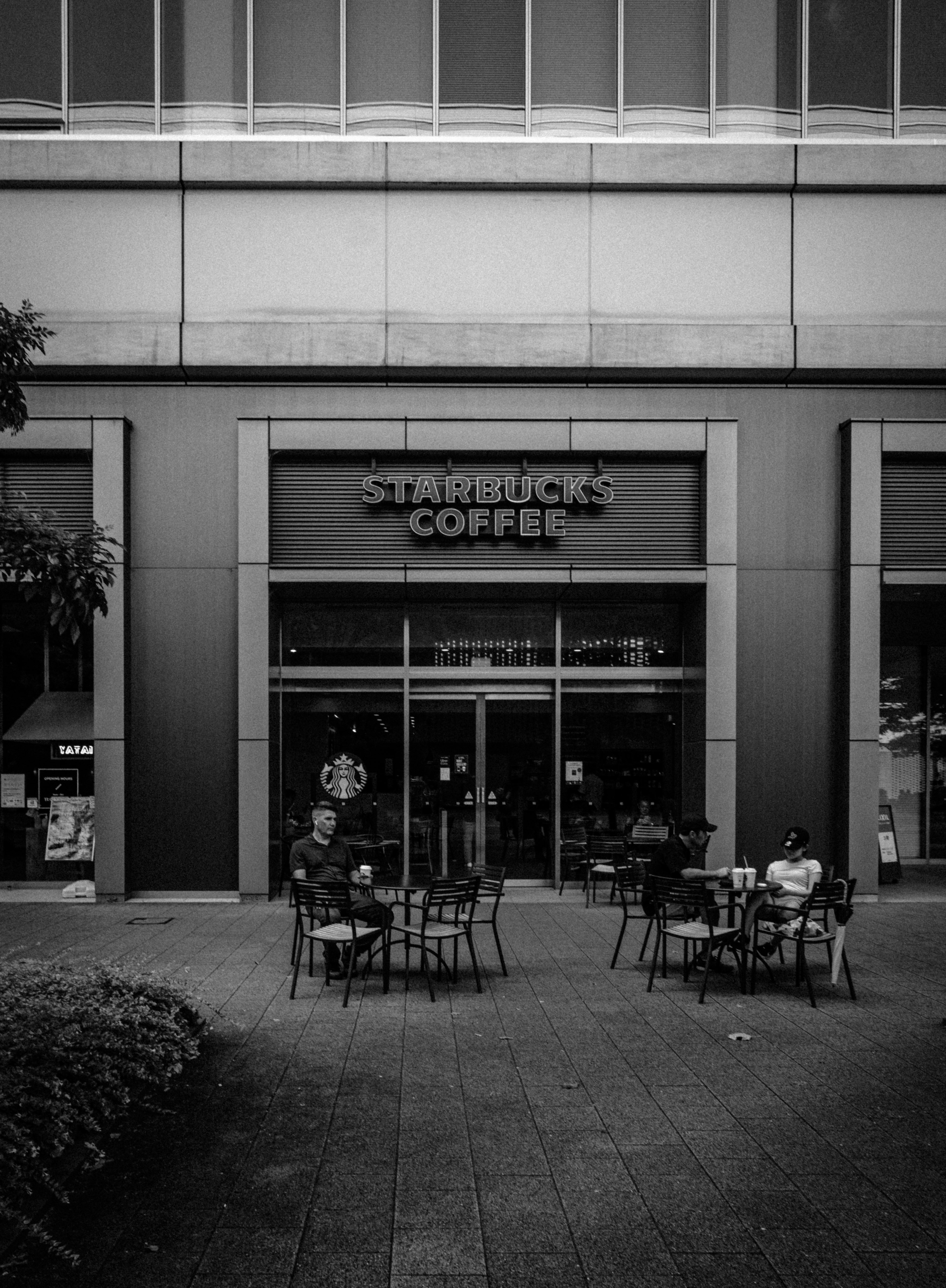 Foto en blanco y negro de una tienda Starbucks Coffee con mesas y sillas al aire libre