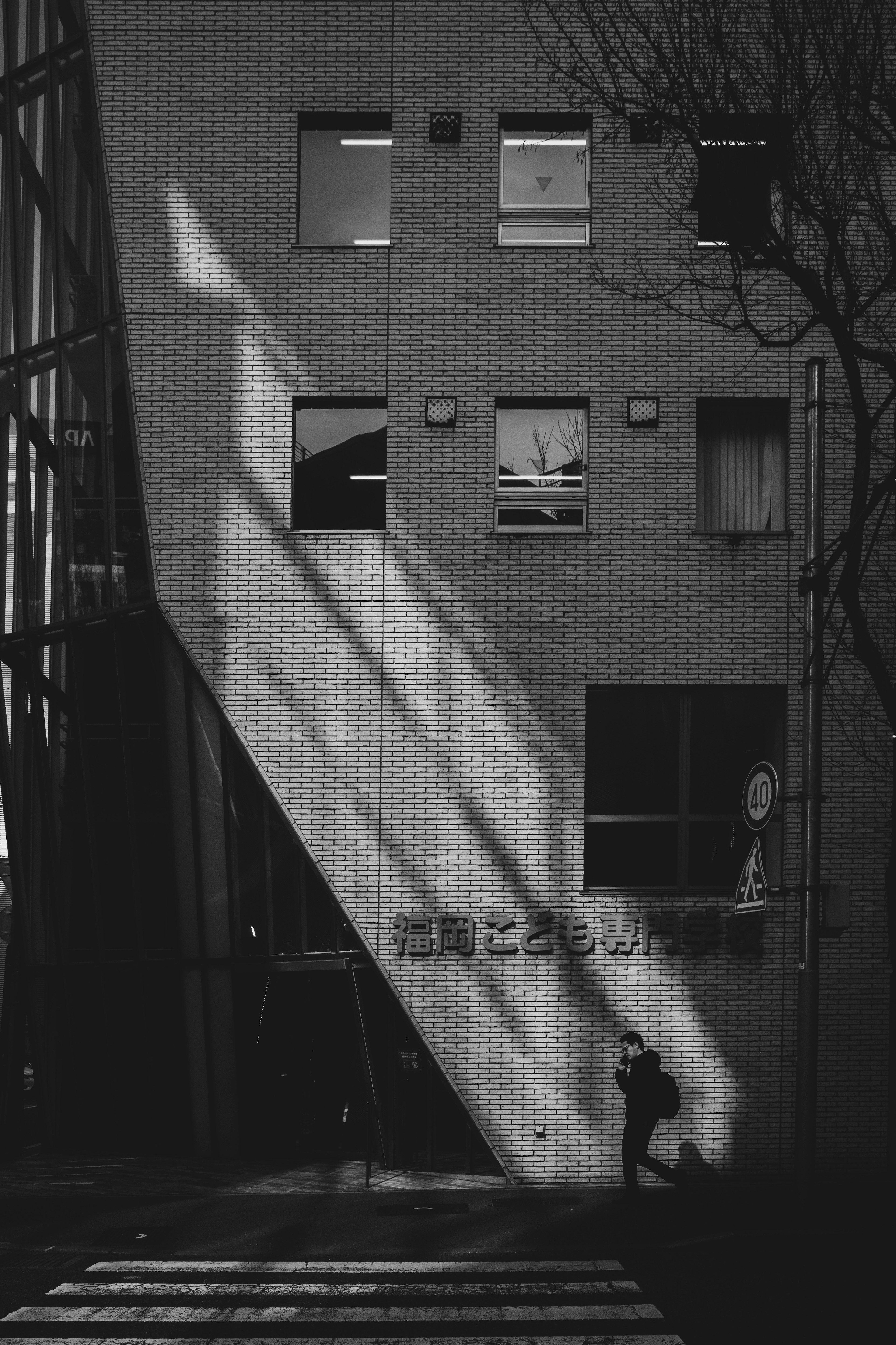 Exterior de un edificio con sombras y una persona caminando en el paso de peatones