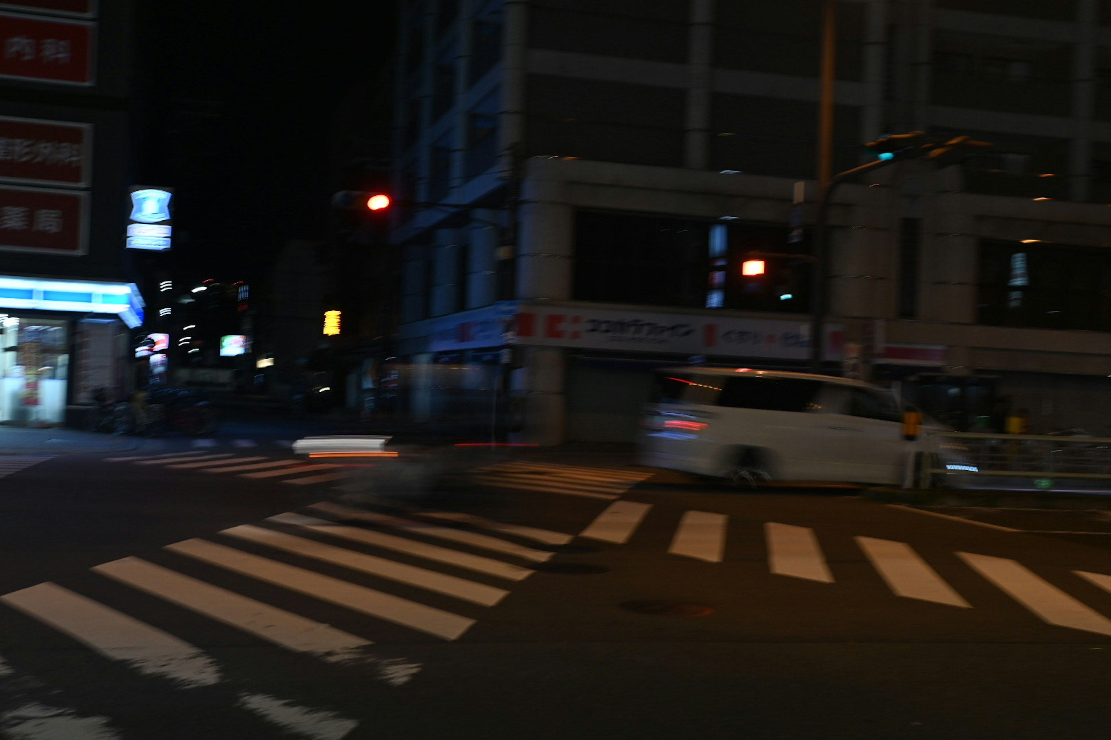 Nighttime intersection with crosswalk visible traffic lights and a passing vehicle