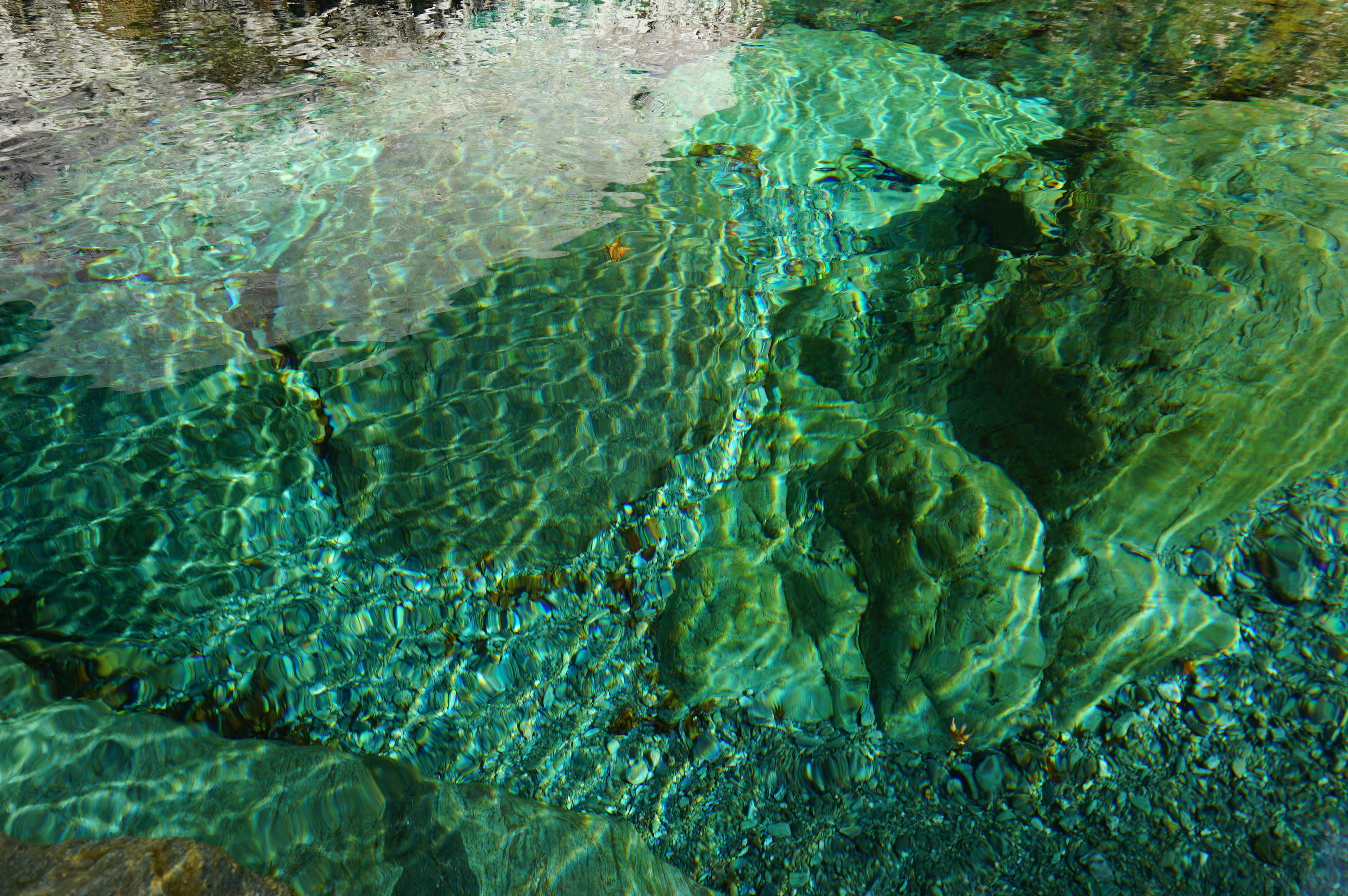 Green rocks visible under clear water with wave reflections