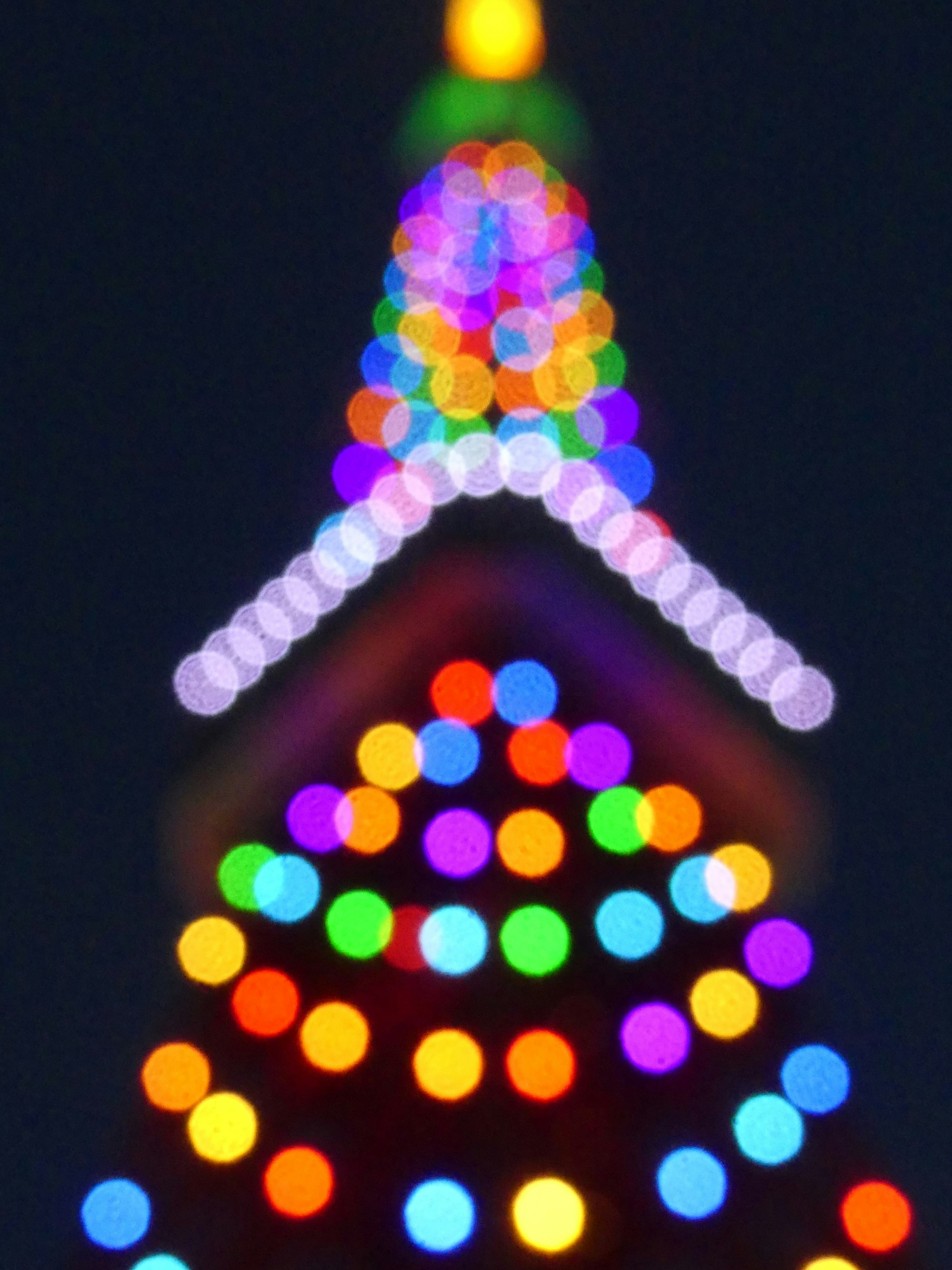 Blurry top of a Christmas tree adorned with vibrant colored lights