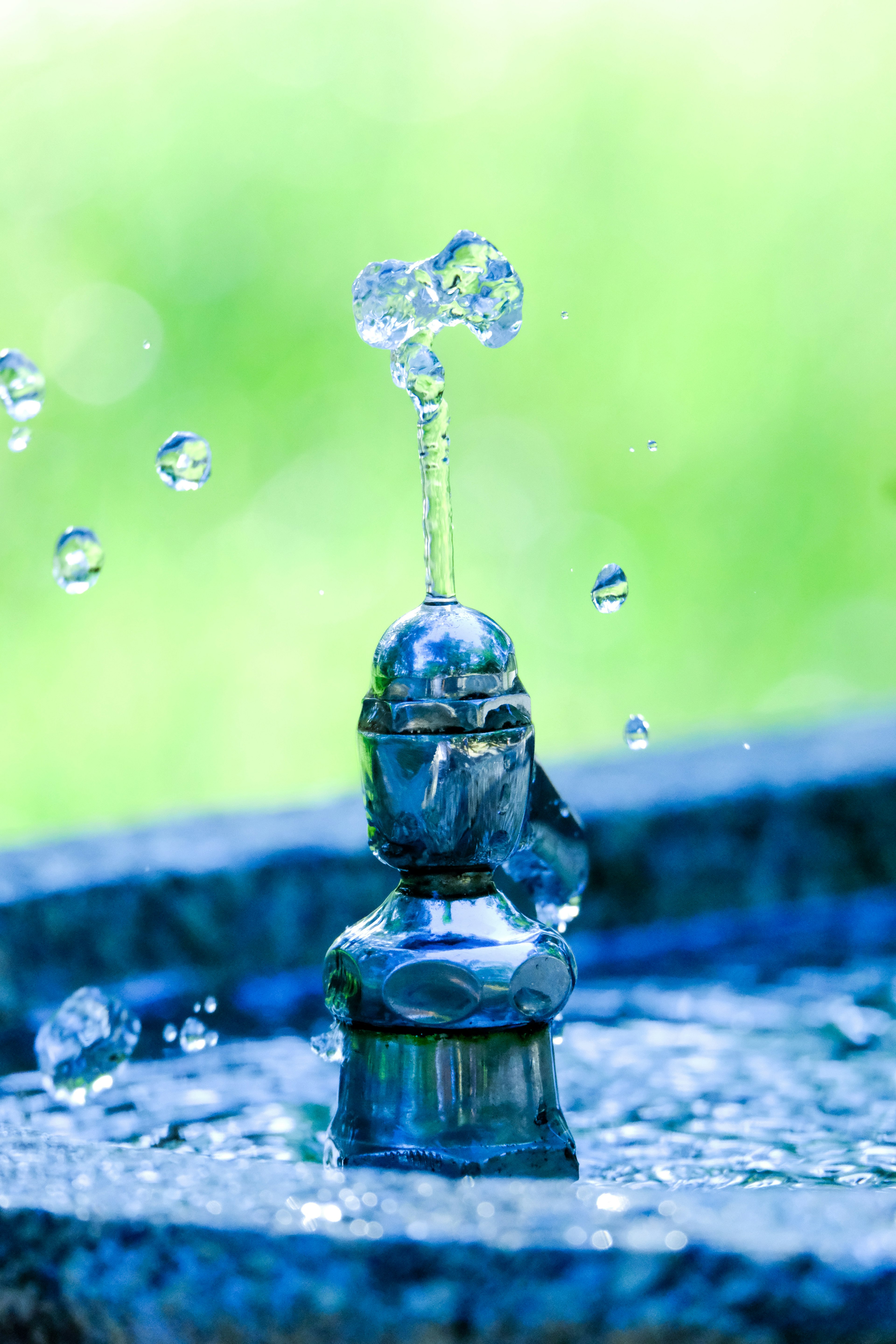 Fontana d'acqua che spruzza gocce d'acqua su uno sfondo verde sfocato che evidenzia un'estetica pulita