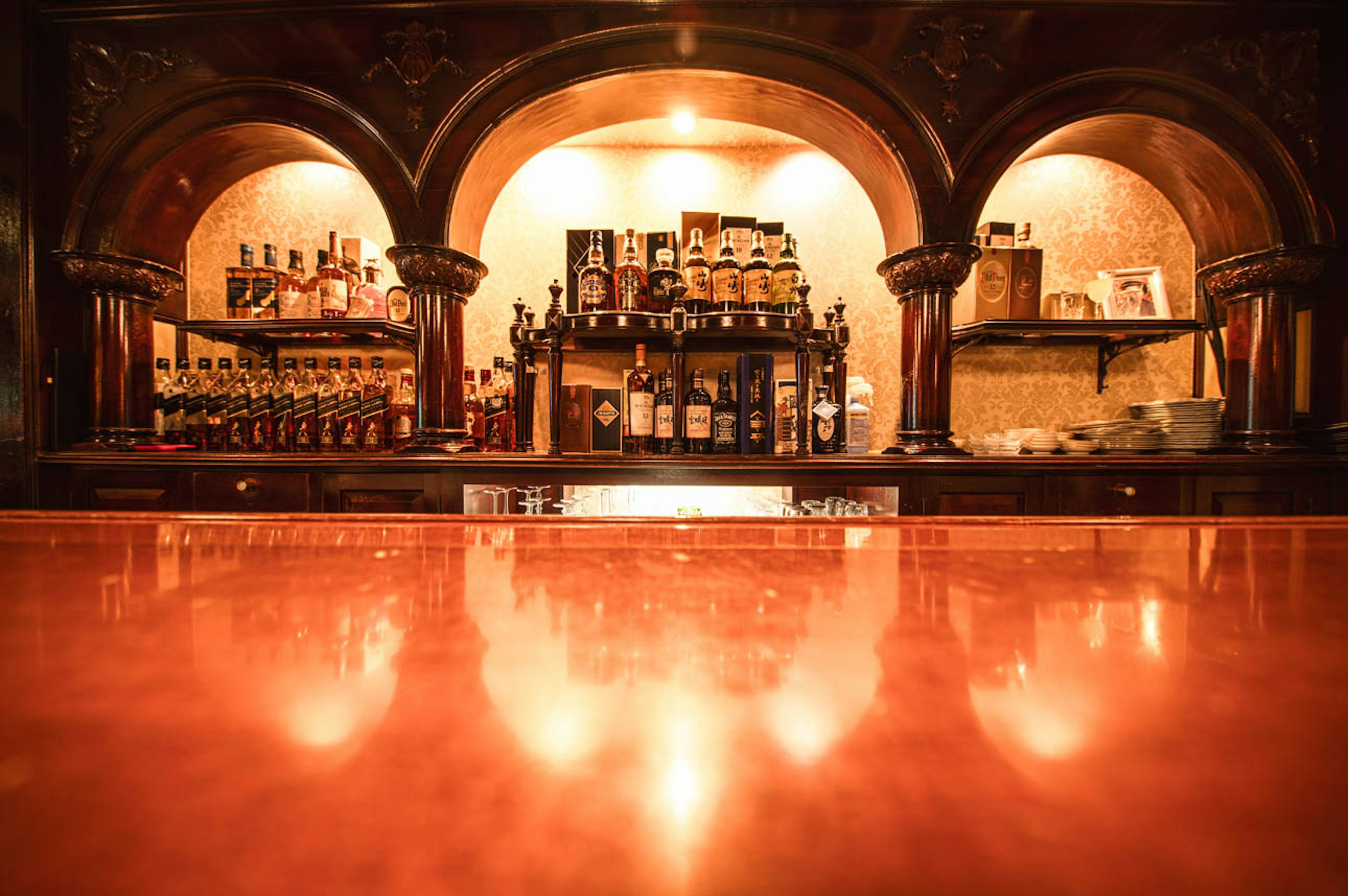 Warm ambiance of a bar with a polished counter and shelves stocked with bottles