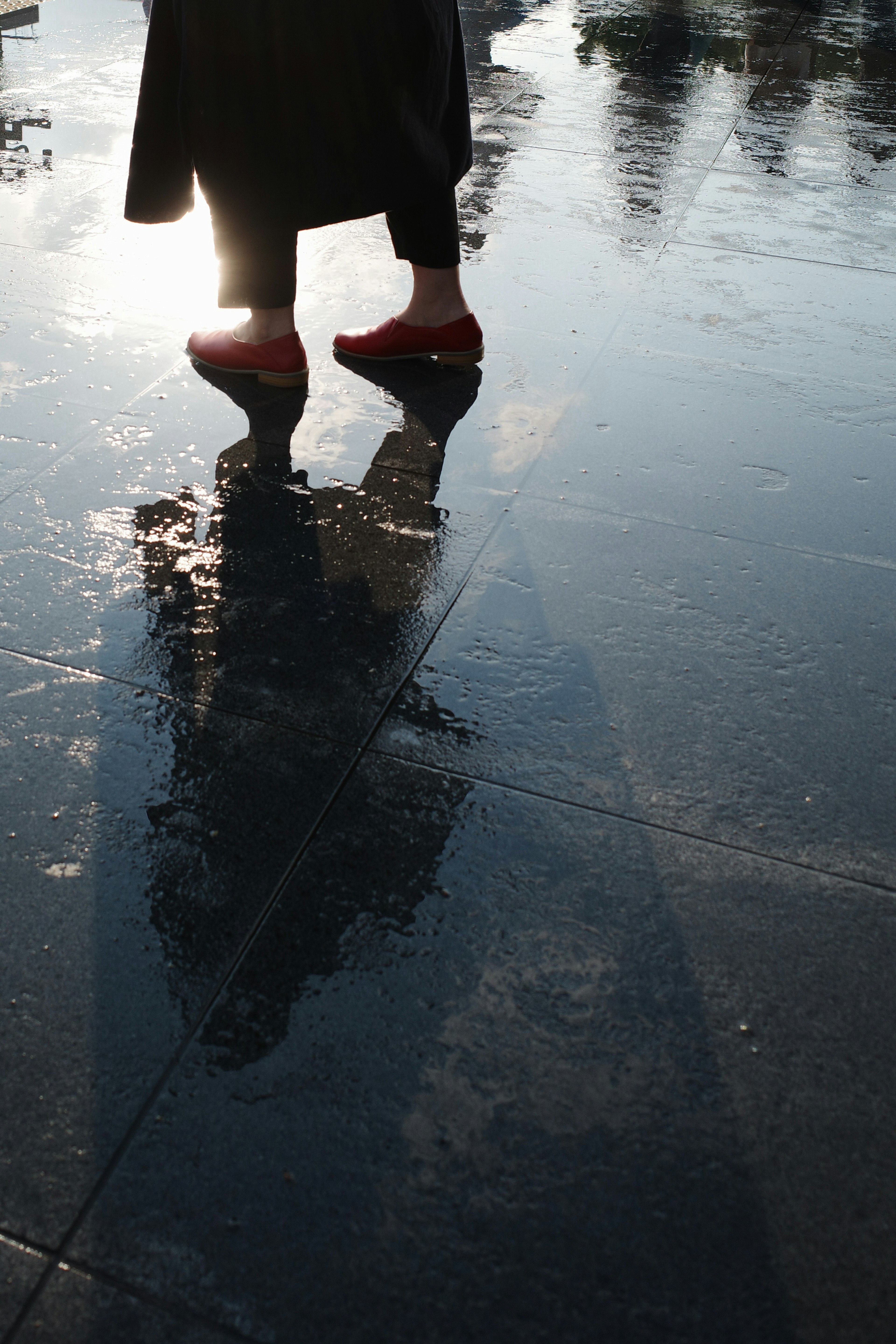 Reflejo de una persona con zapatos rojos en una superficie mojada con luz solar