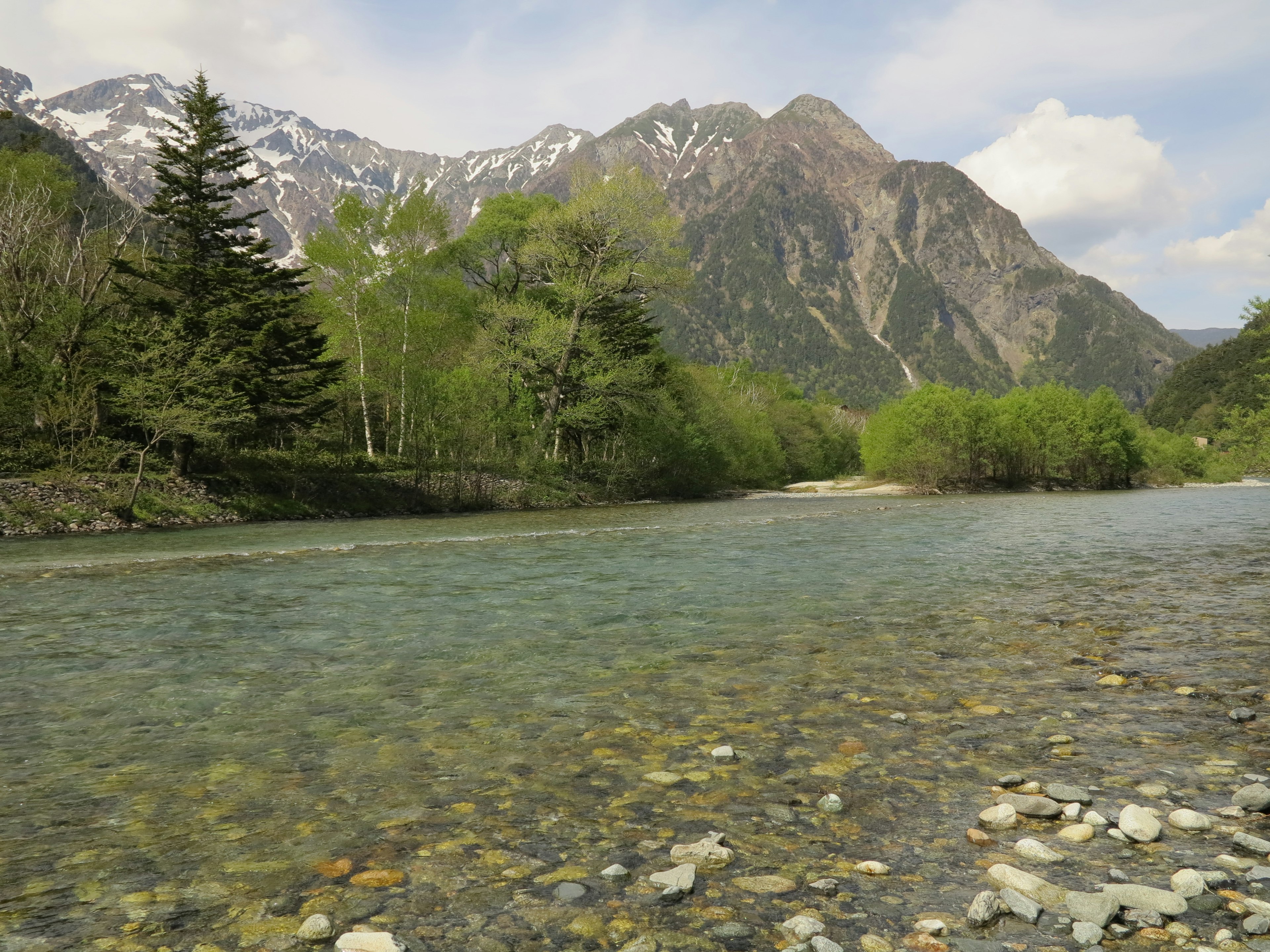 Pemandangan sungai jernih dikelilingi pepohonan hijau dan pegunungan