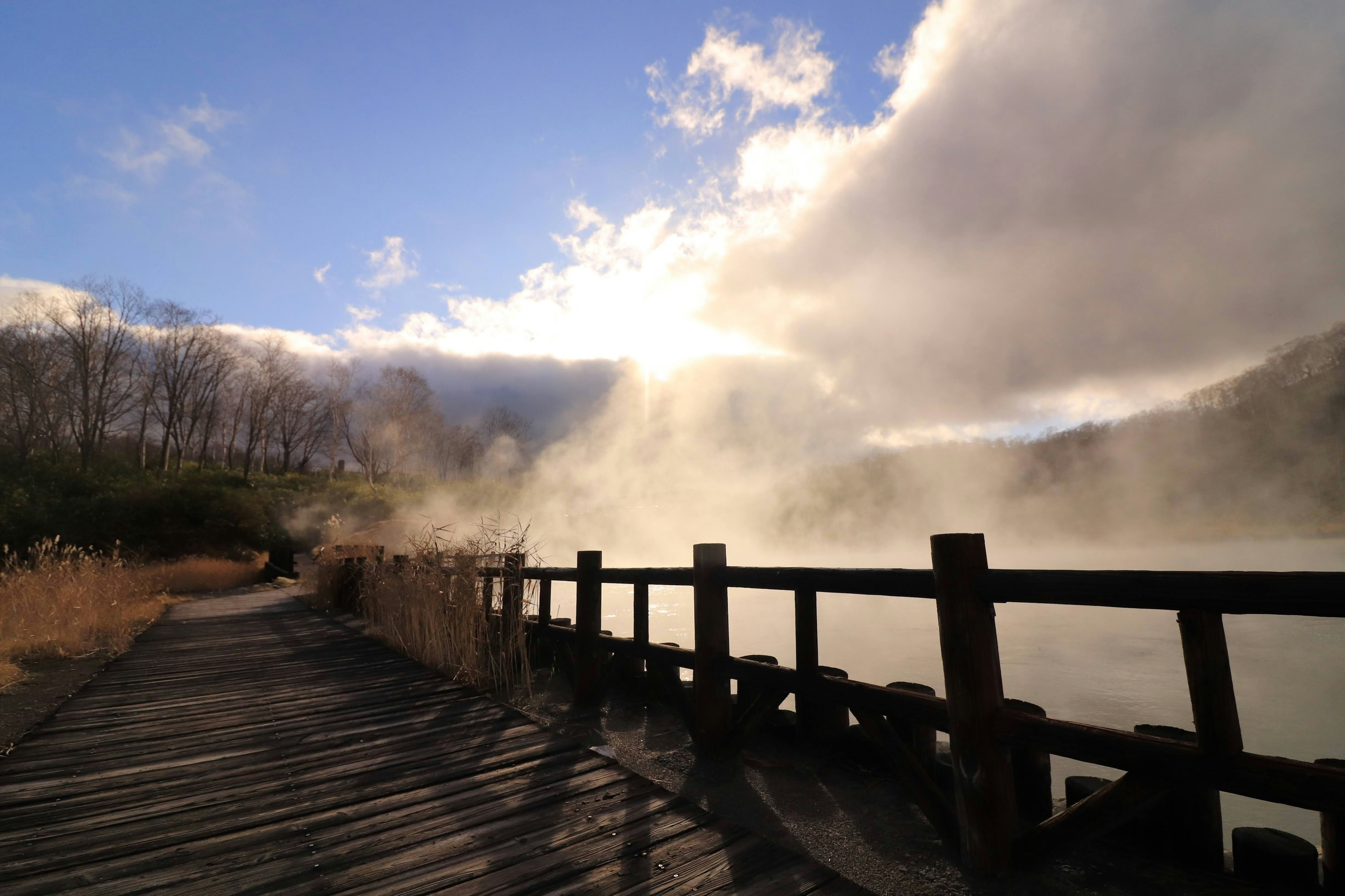 Sentiero in legno vicino a un lago nebbioso sotto un cielo nuvoloso