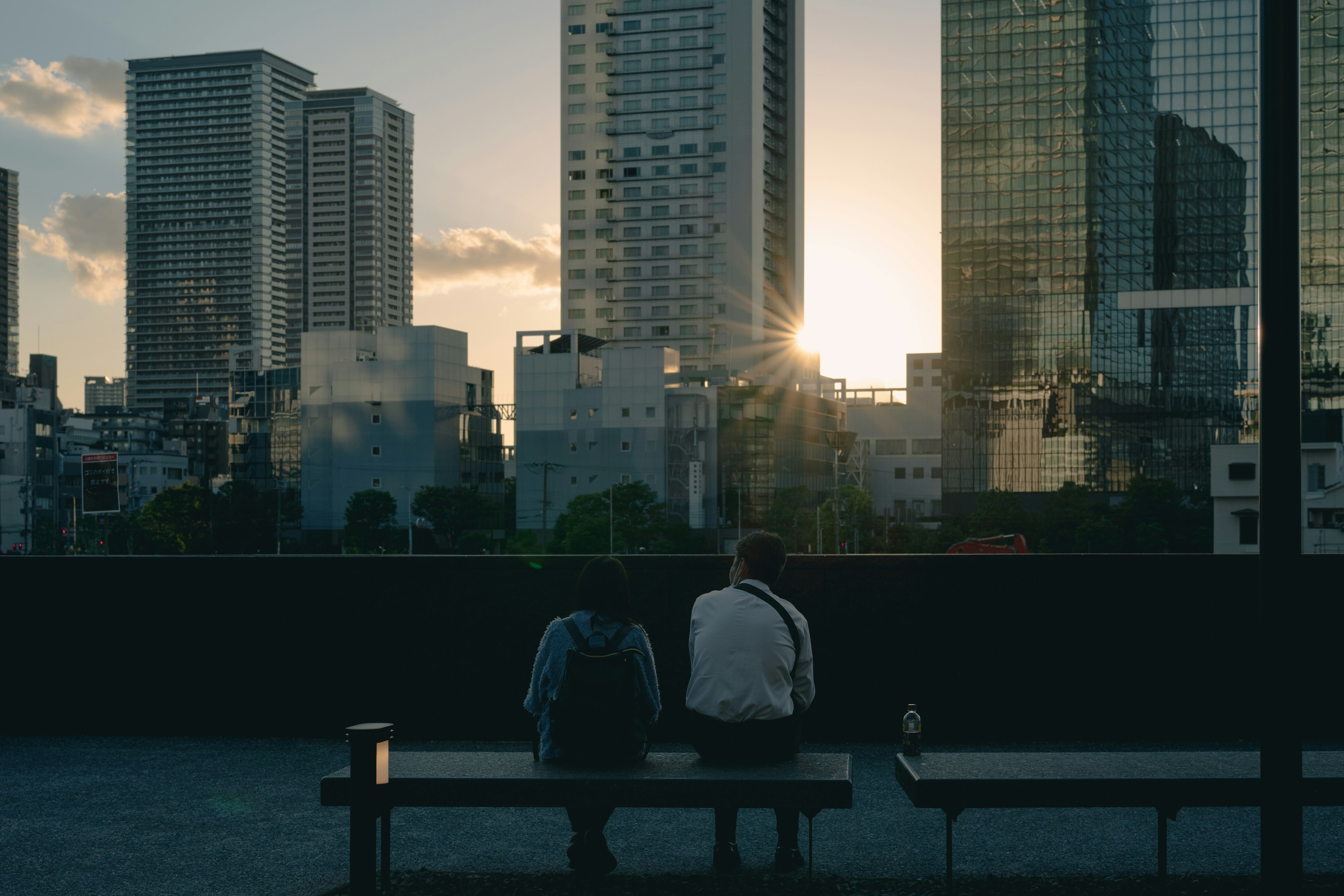 Deux personnes assises sur un banc surplombant une skyline urbaine au coucher du soleil