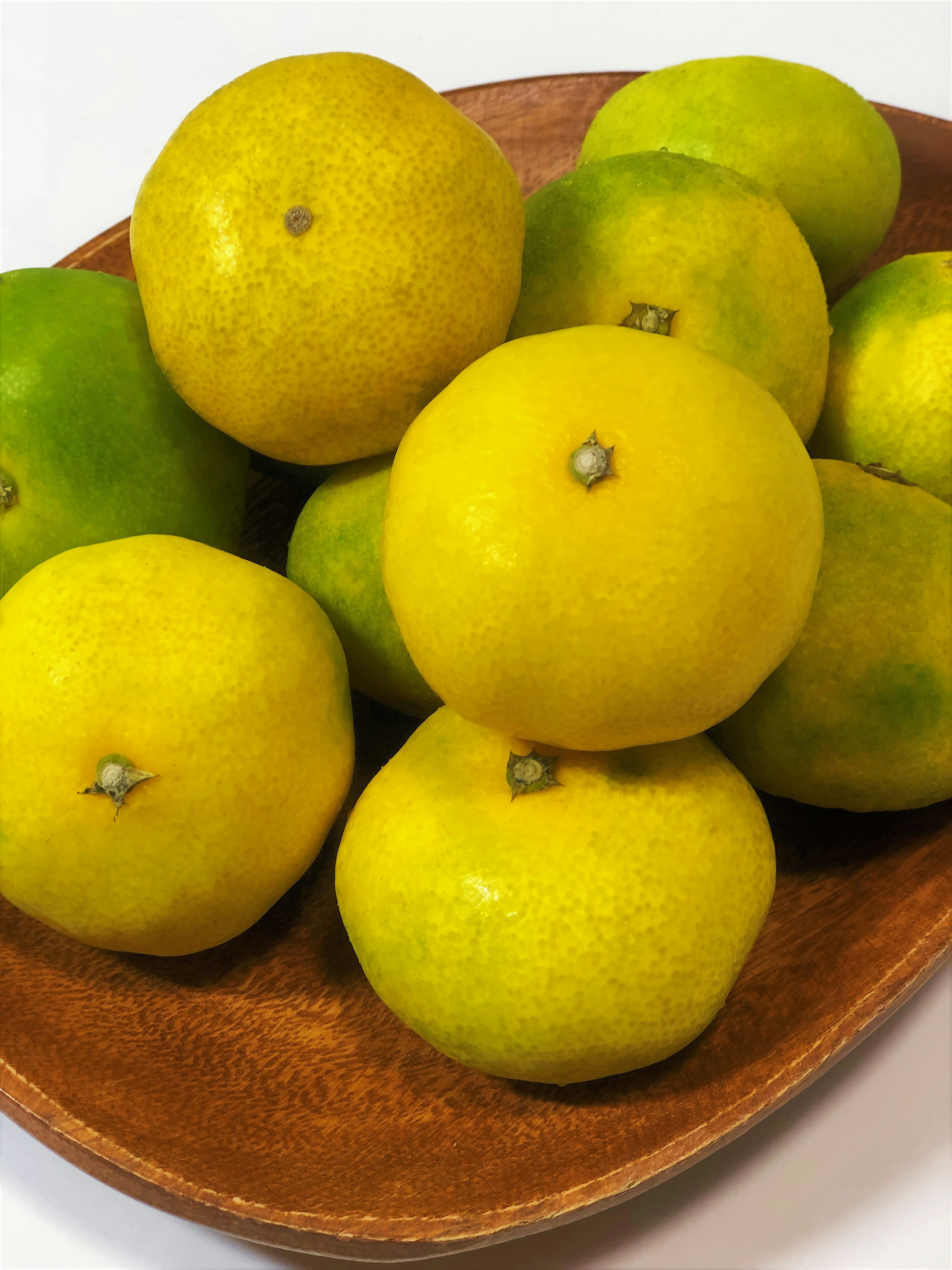 A wooden bowl filled with yellow citrus fruits