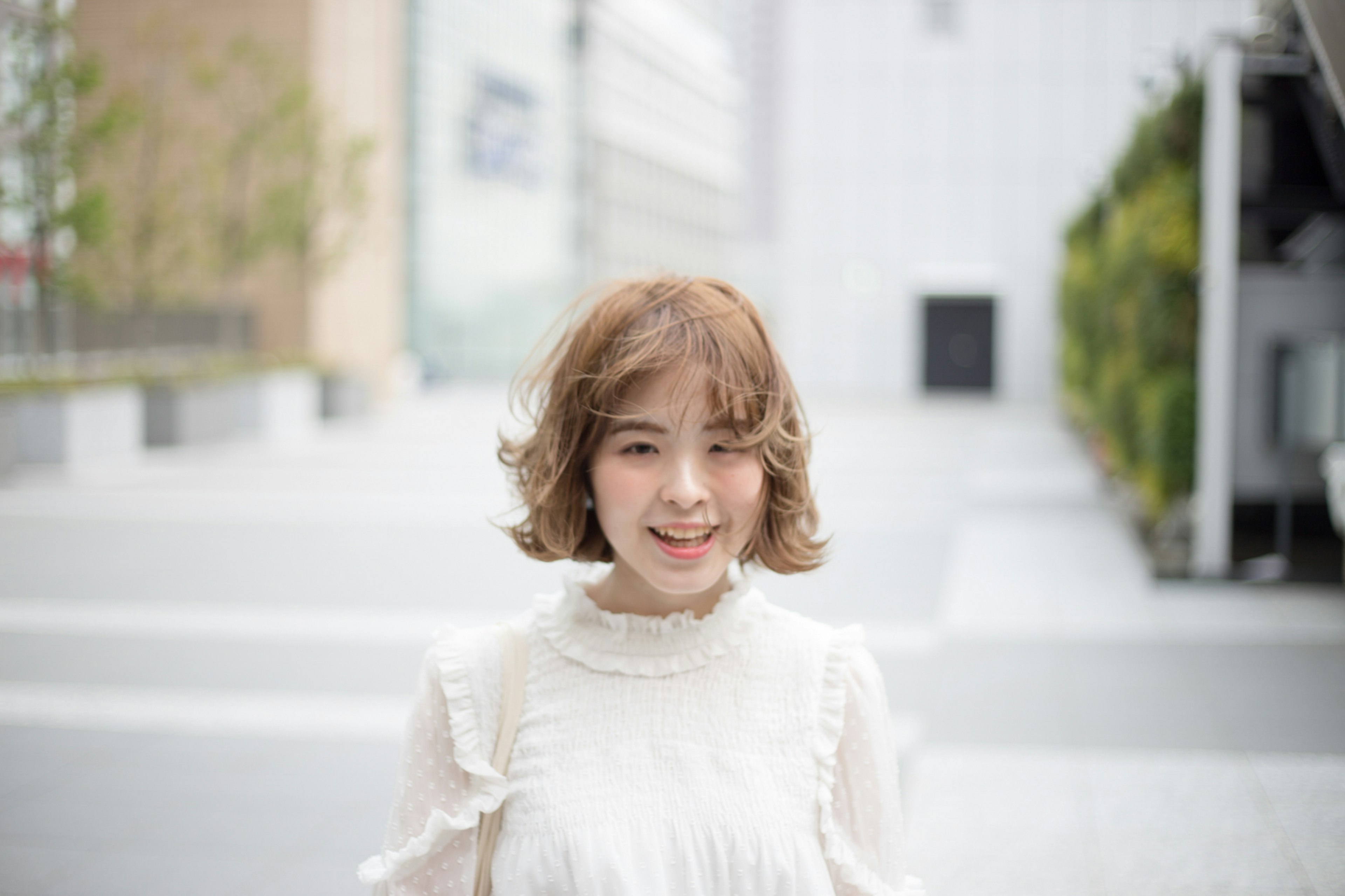 A woman smiling in a white blouse against an urban background