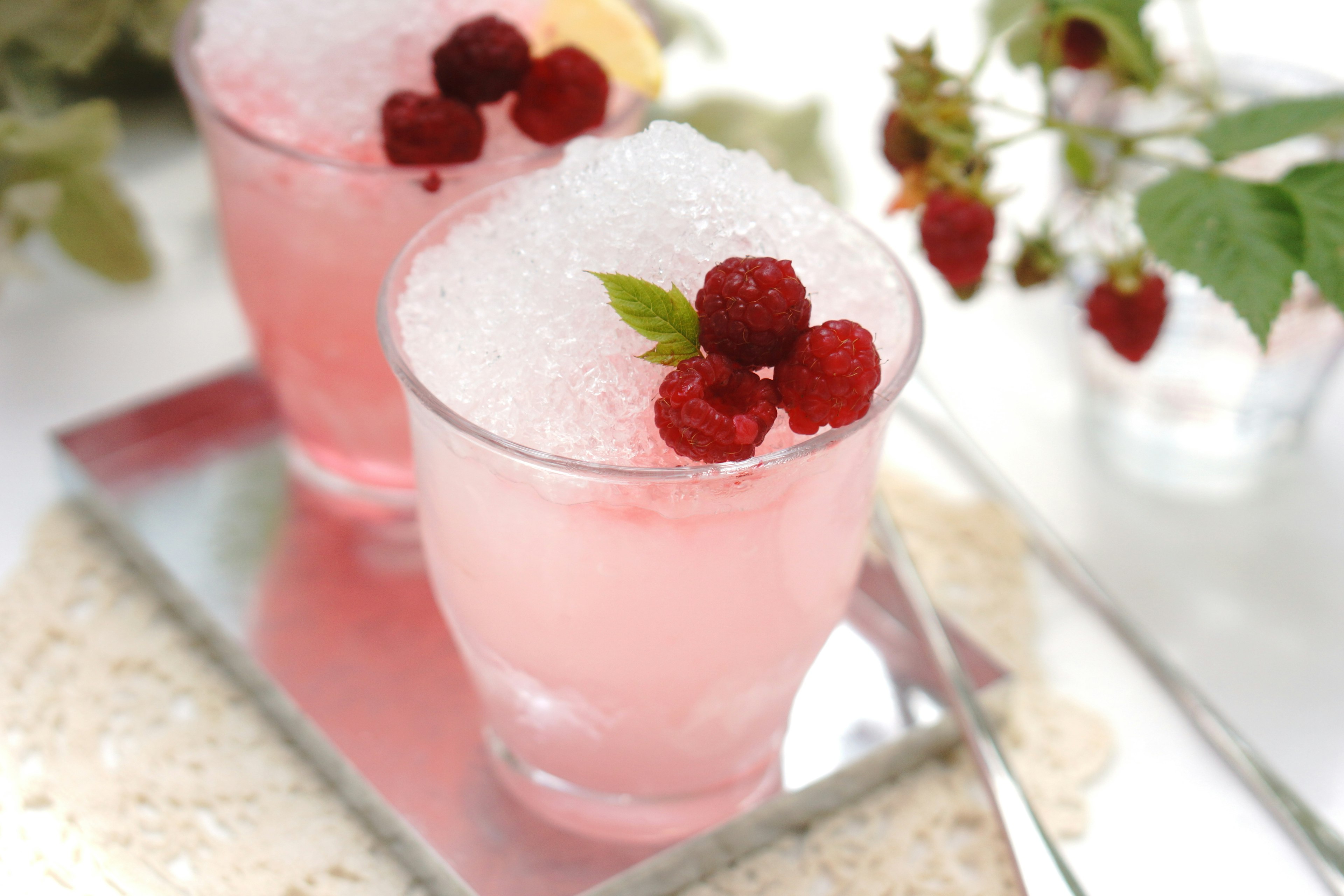 Deux boissons roses servies avec de la glace pilée garnies de framboises et de feuilles de menthe