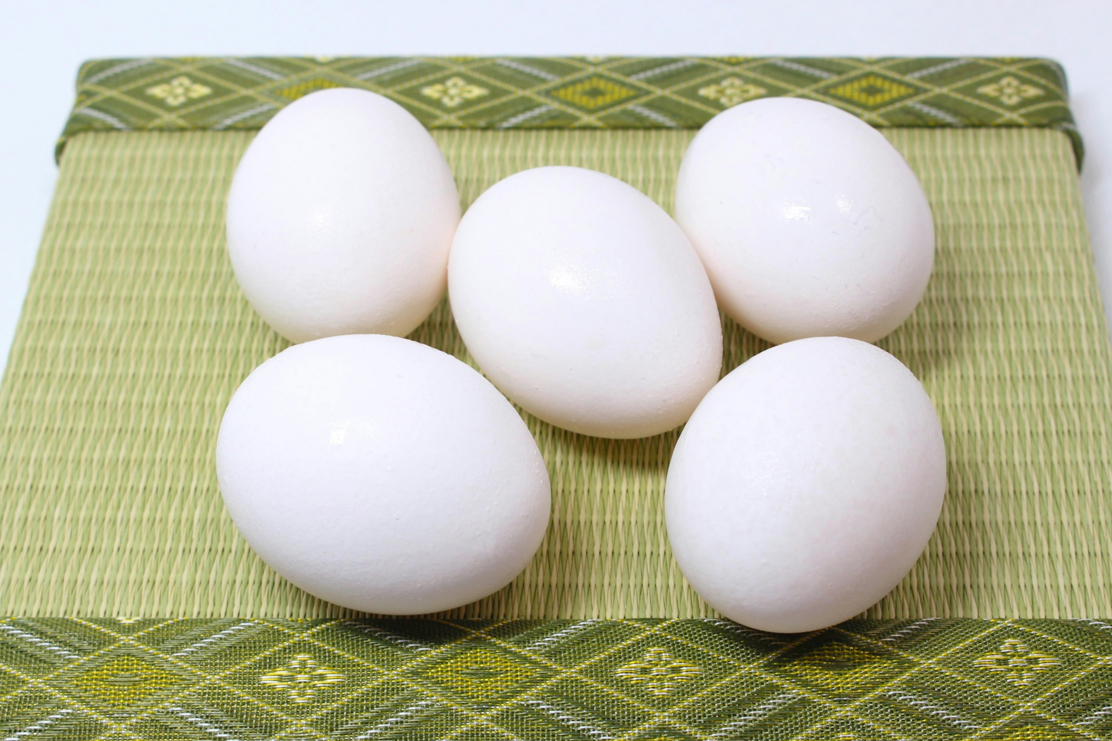 Five white eggs arranged on a green mat