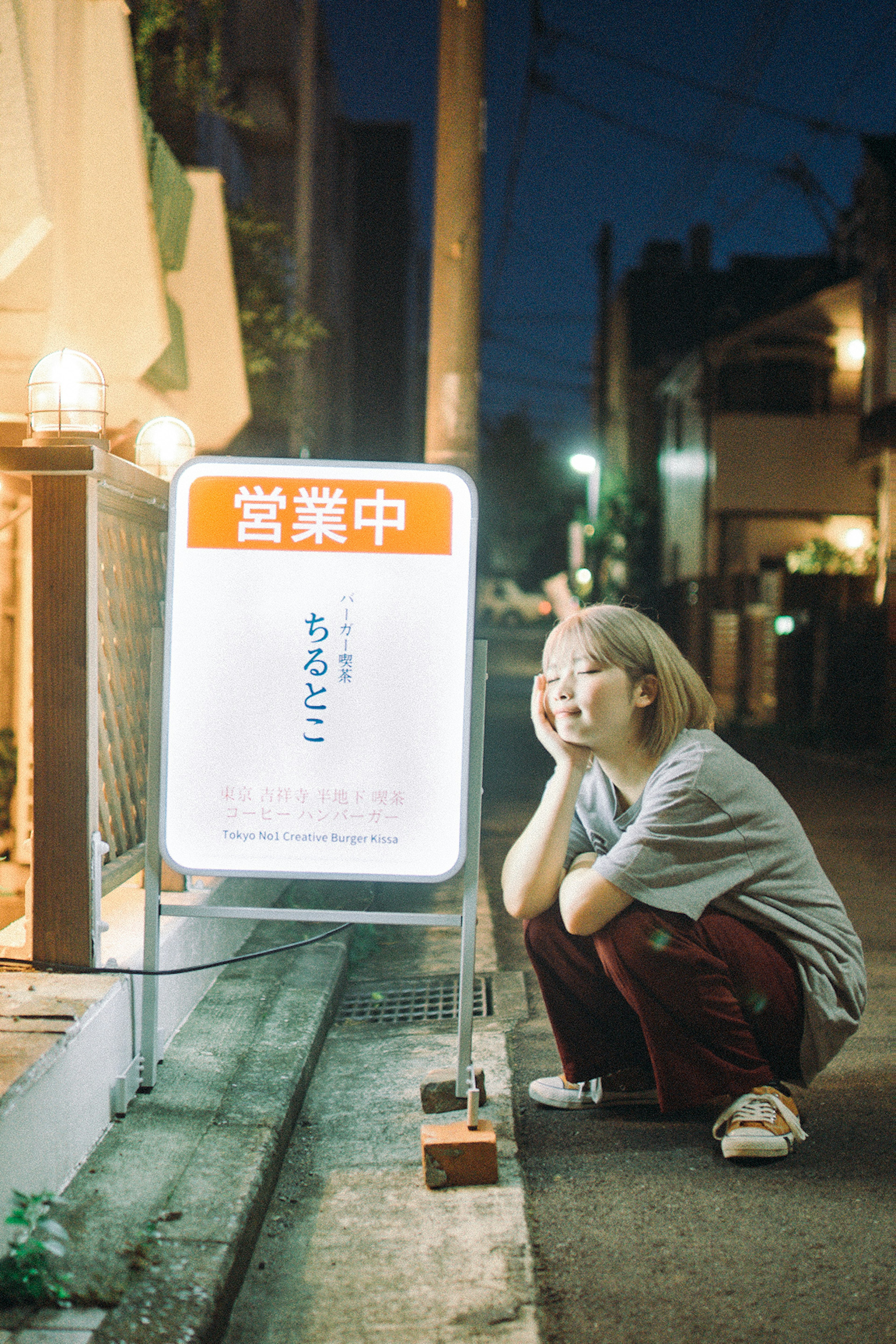 夜の街角で座っている女性と明るい看板