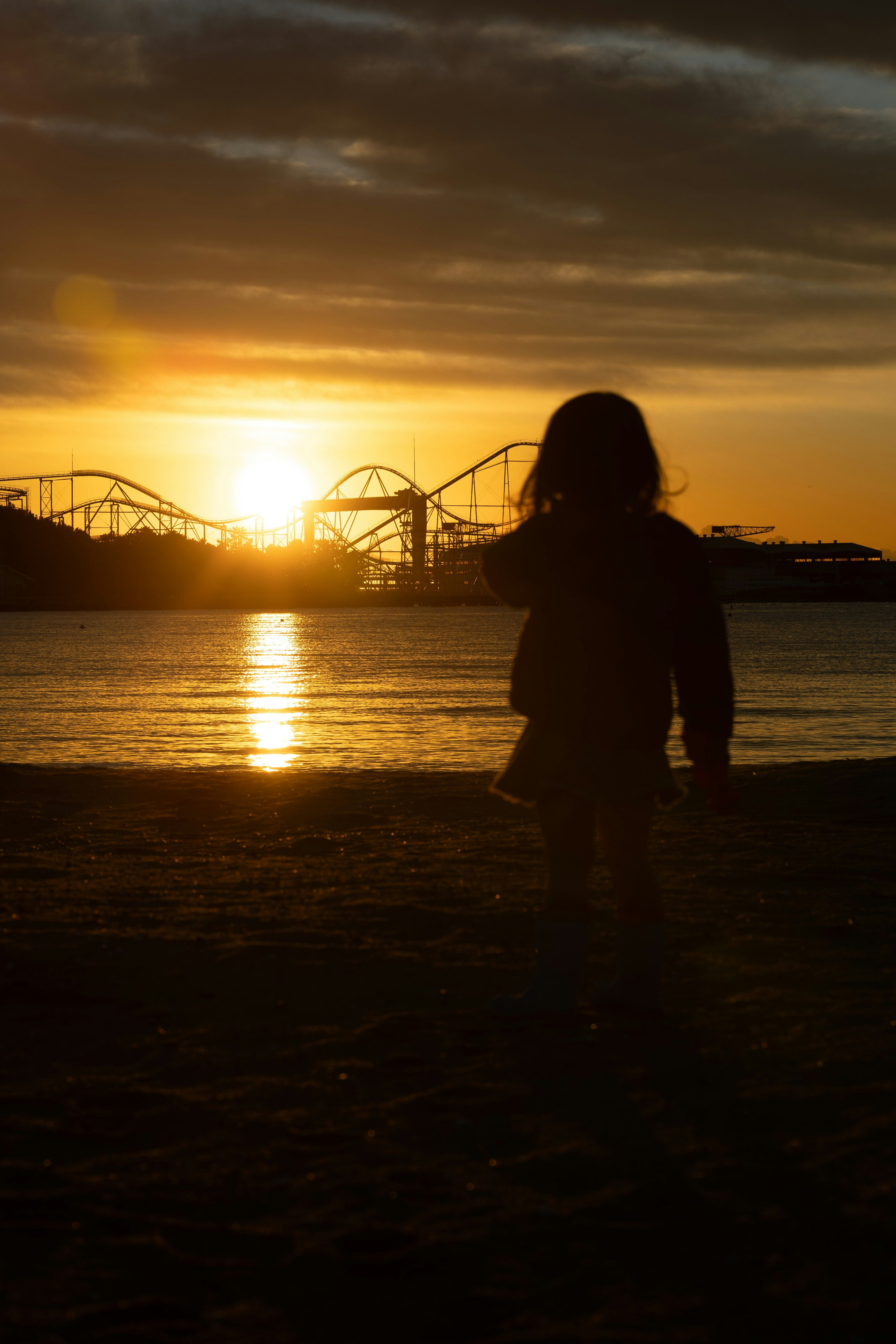 Silhouette d'un enfant contre le coucher de soleil Scène de plage avec montagnes russes d'un parc d'attractions au loin