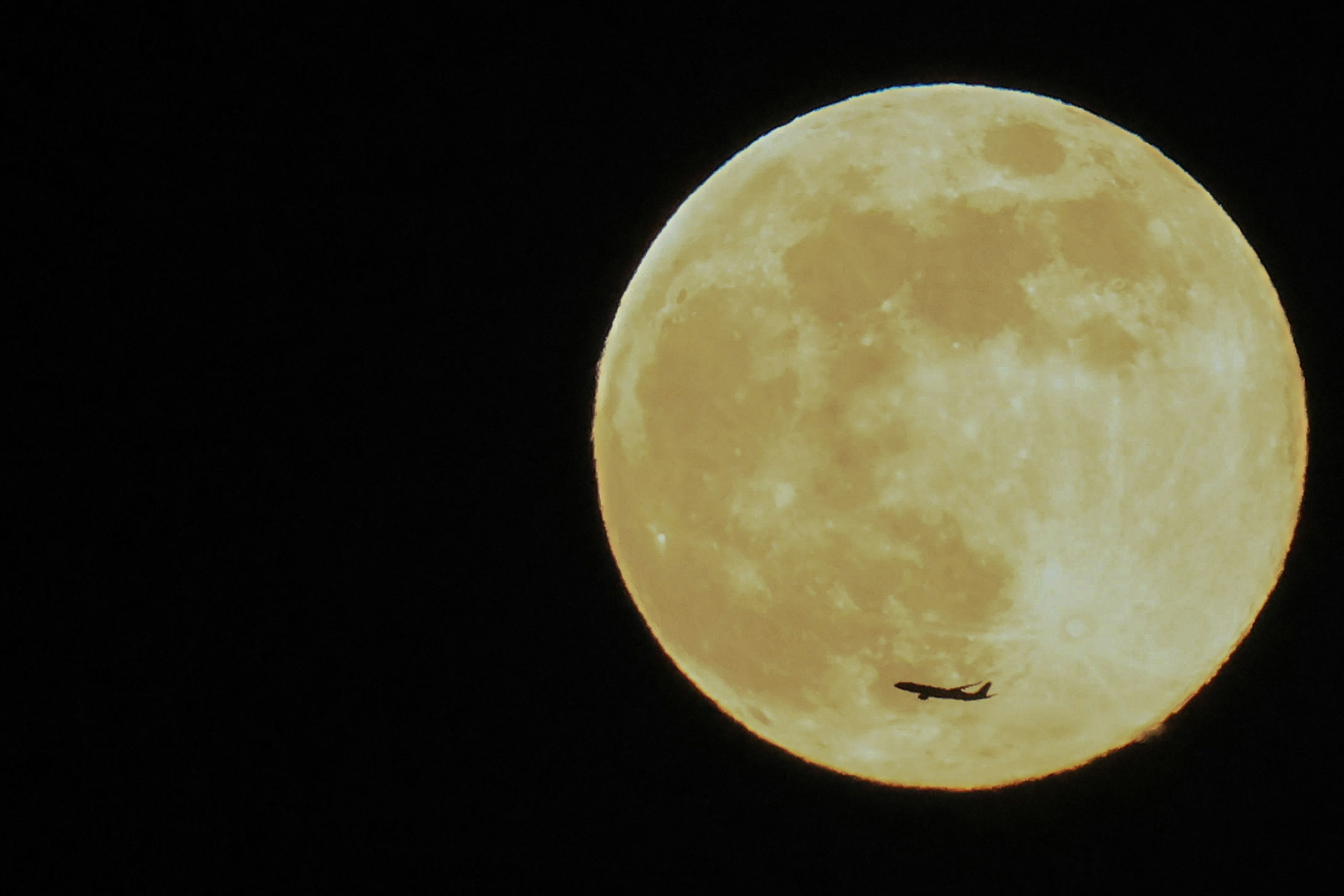 満月の前を飛ぶ航空機のシルエット