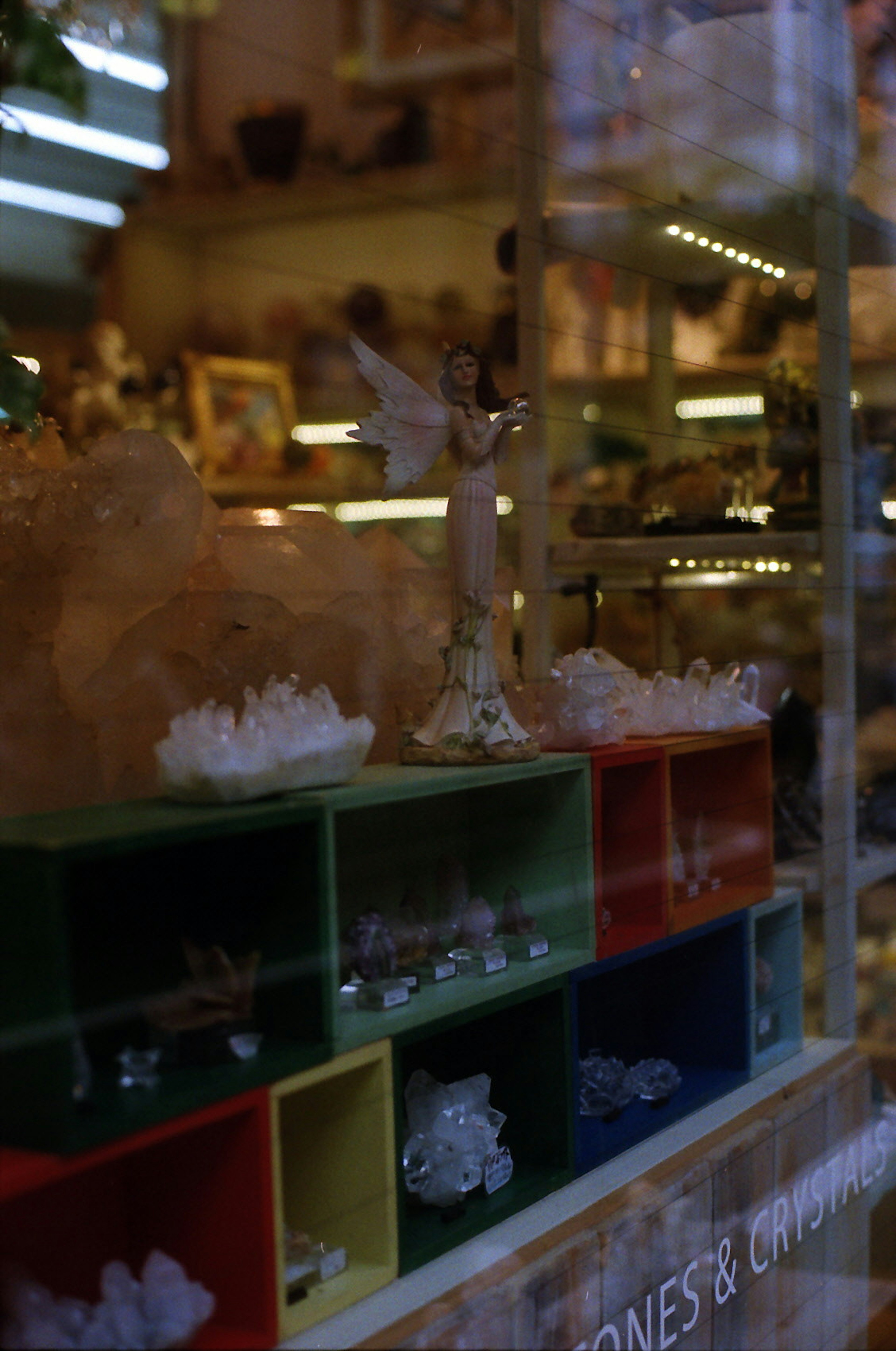 Figurine d'ange exposée dans une vitrine de magasin avec des étagères colorées de cristaux et de pierres précieuses