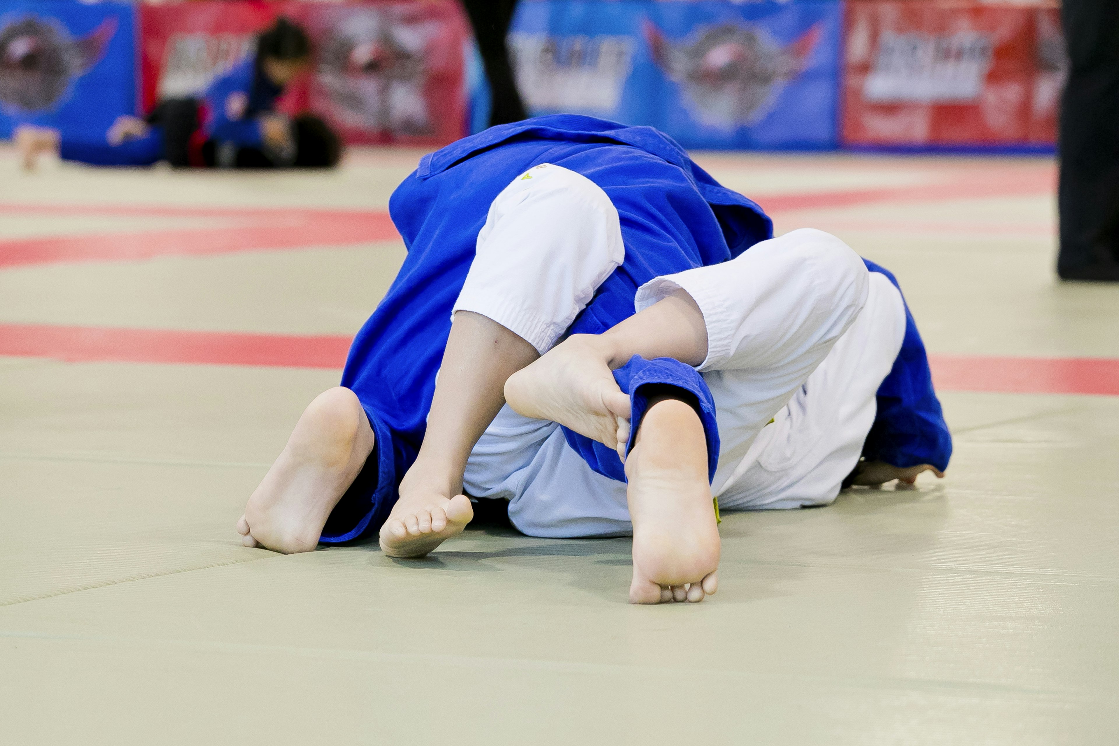 Two judokas in blue and white uniforms grappling on a mat