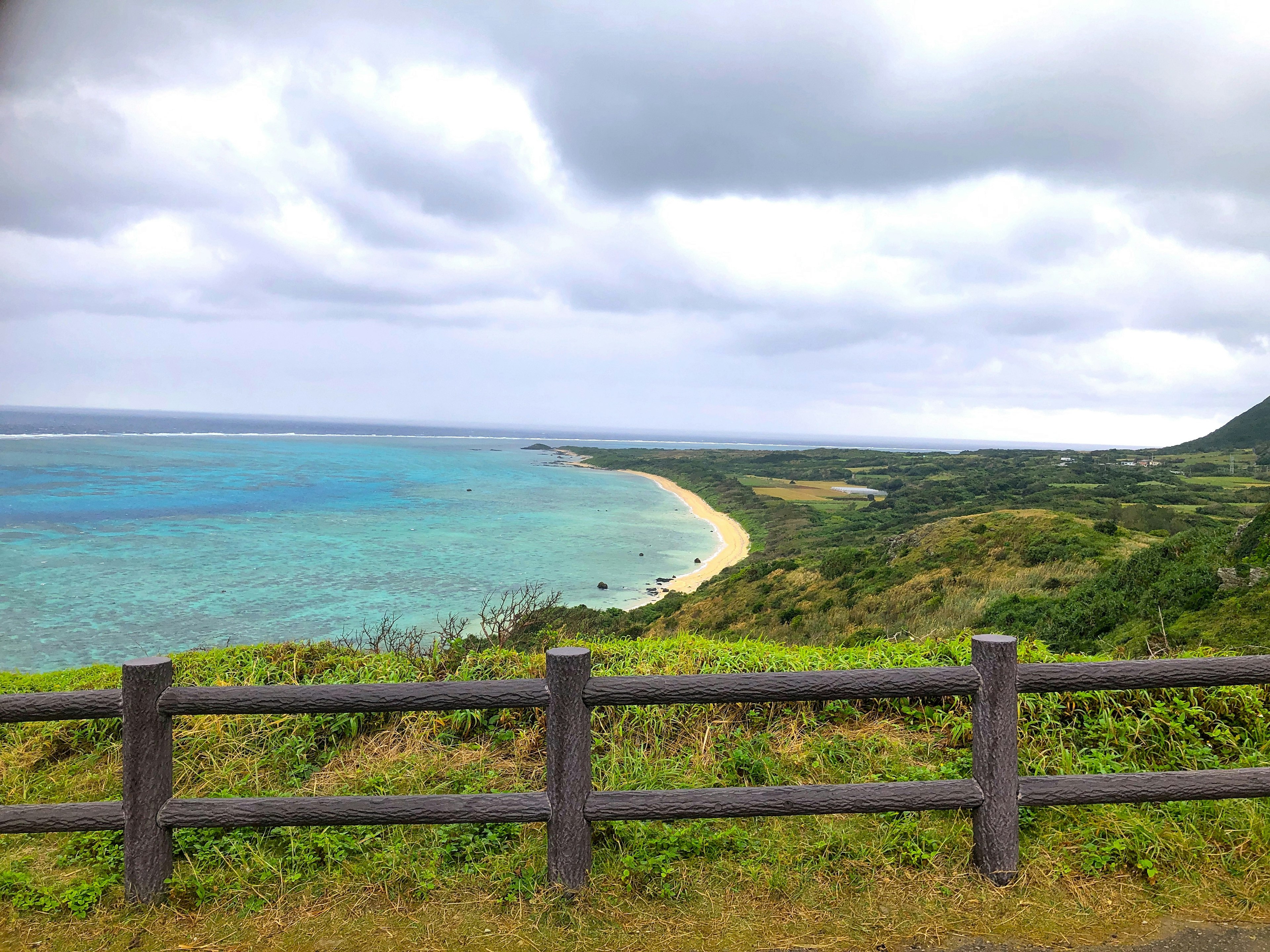 青い海と緑の丘が広がる風景に木製のフェンスがある