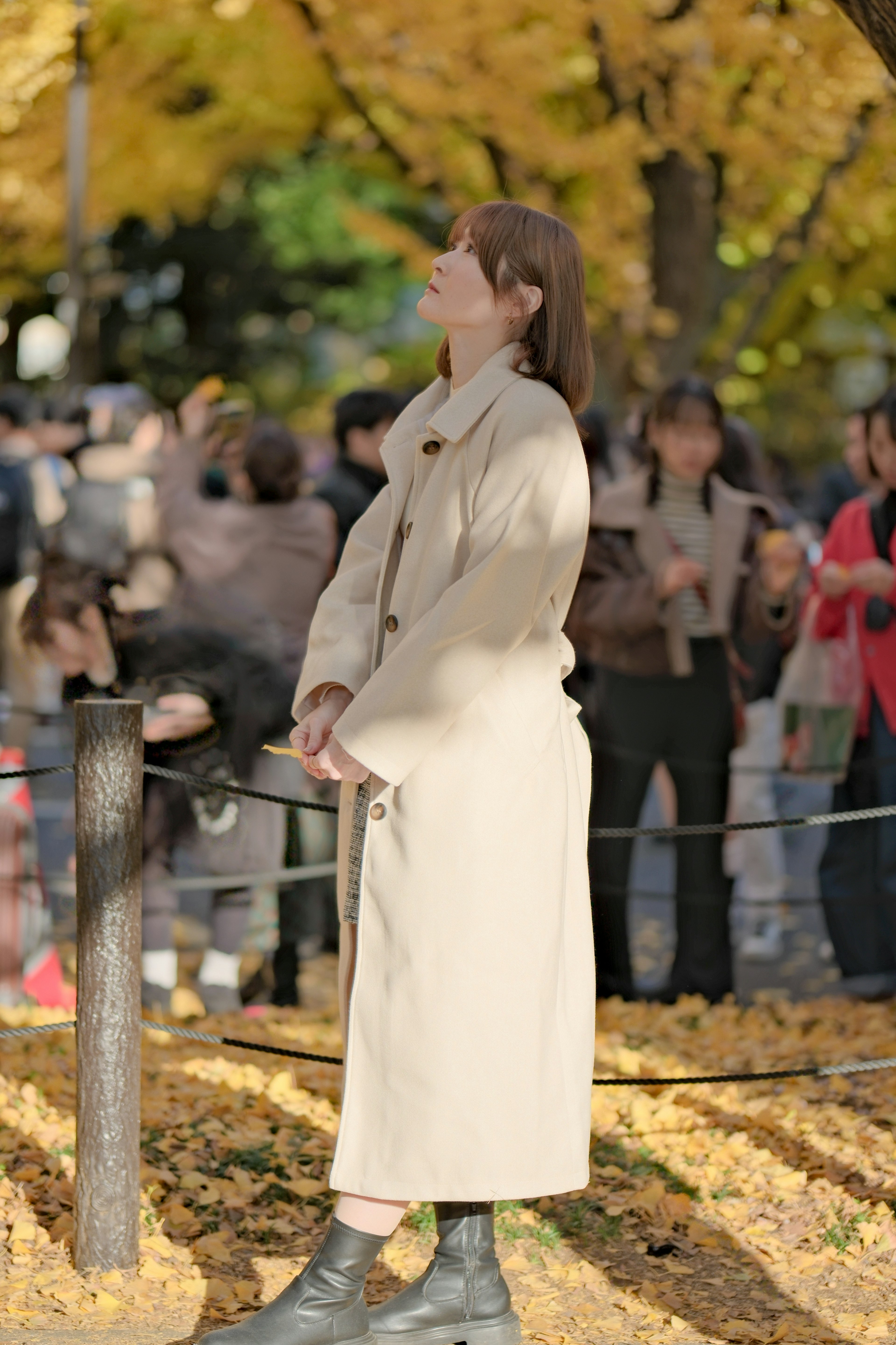 秋の公園で立っている女性の後ろ姿 黄色い葉が散らばる背景