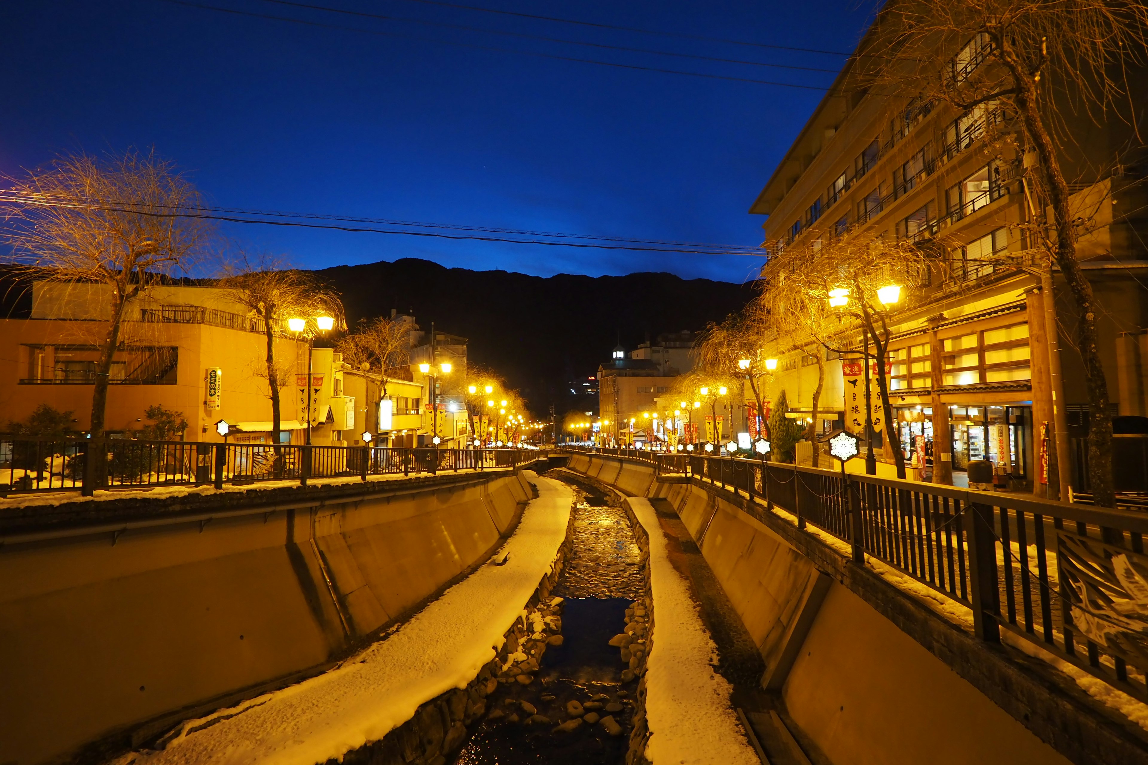 Vue nocturne d'une rue au bord de la rivière avec des bâtiments illuminés et des rives enneigées