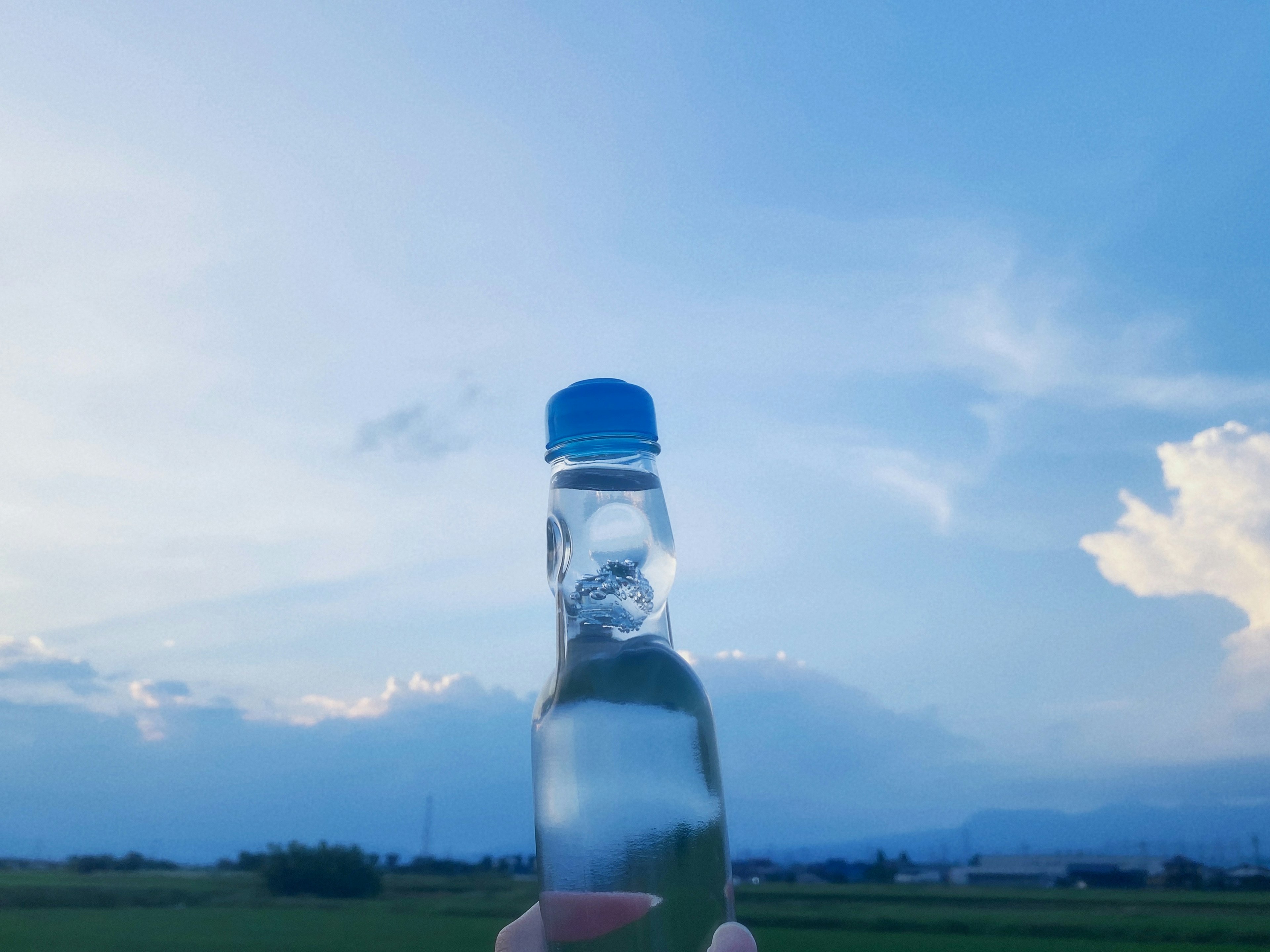 Eine Hand hält eine Wasserflasche vor einem blauen Himmel