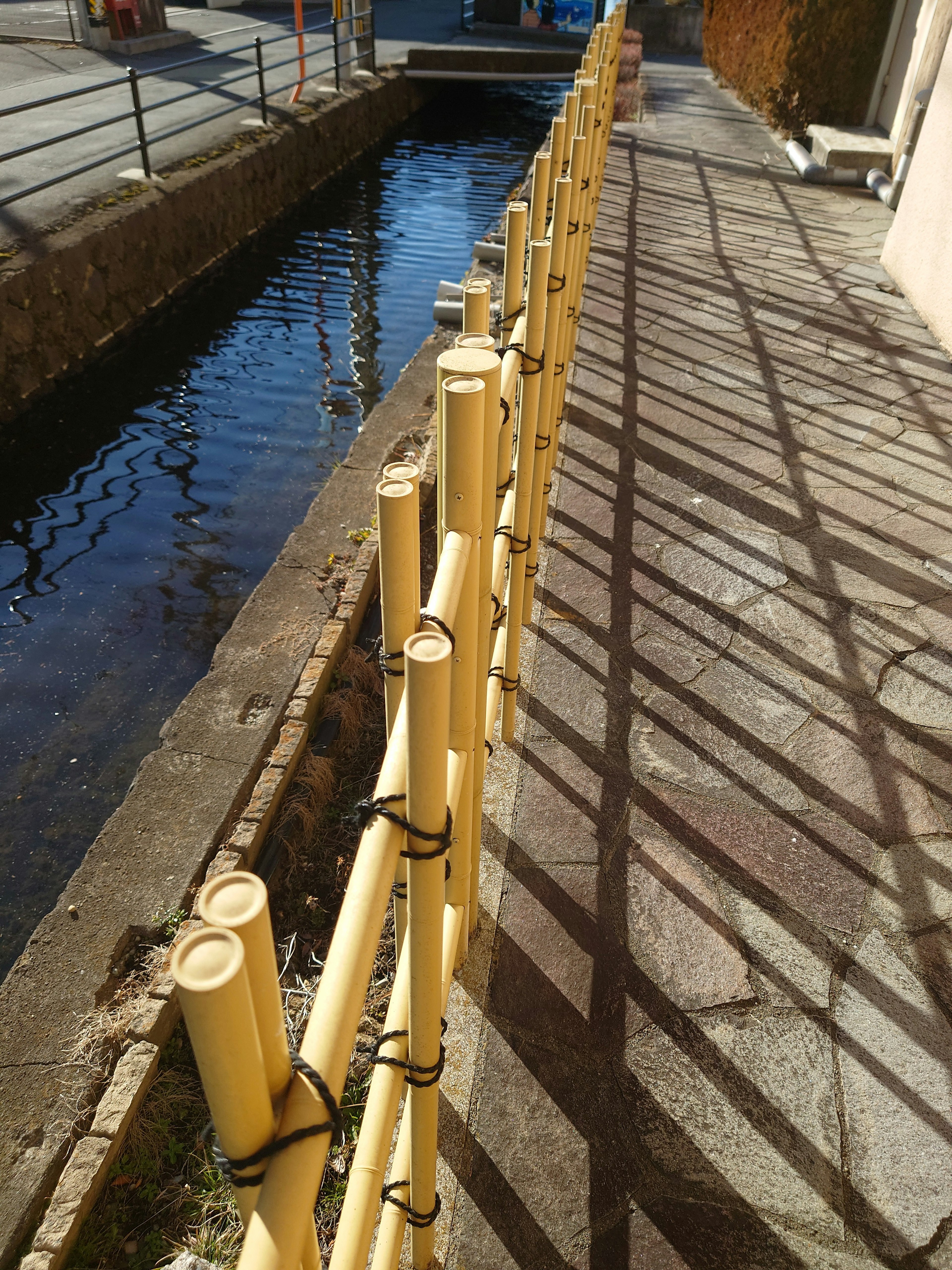 Cerca de bambú amarillo a lo largo de un canal con sombras