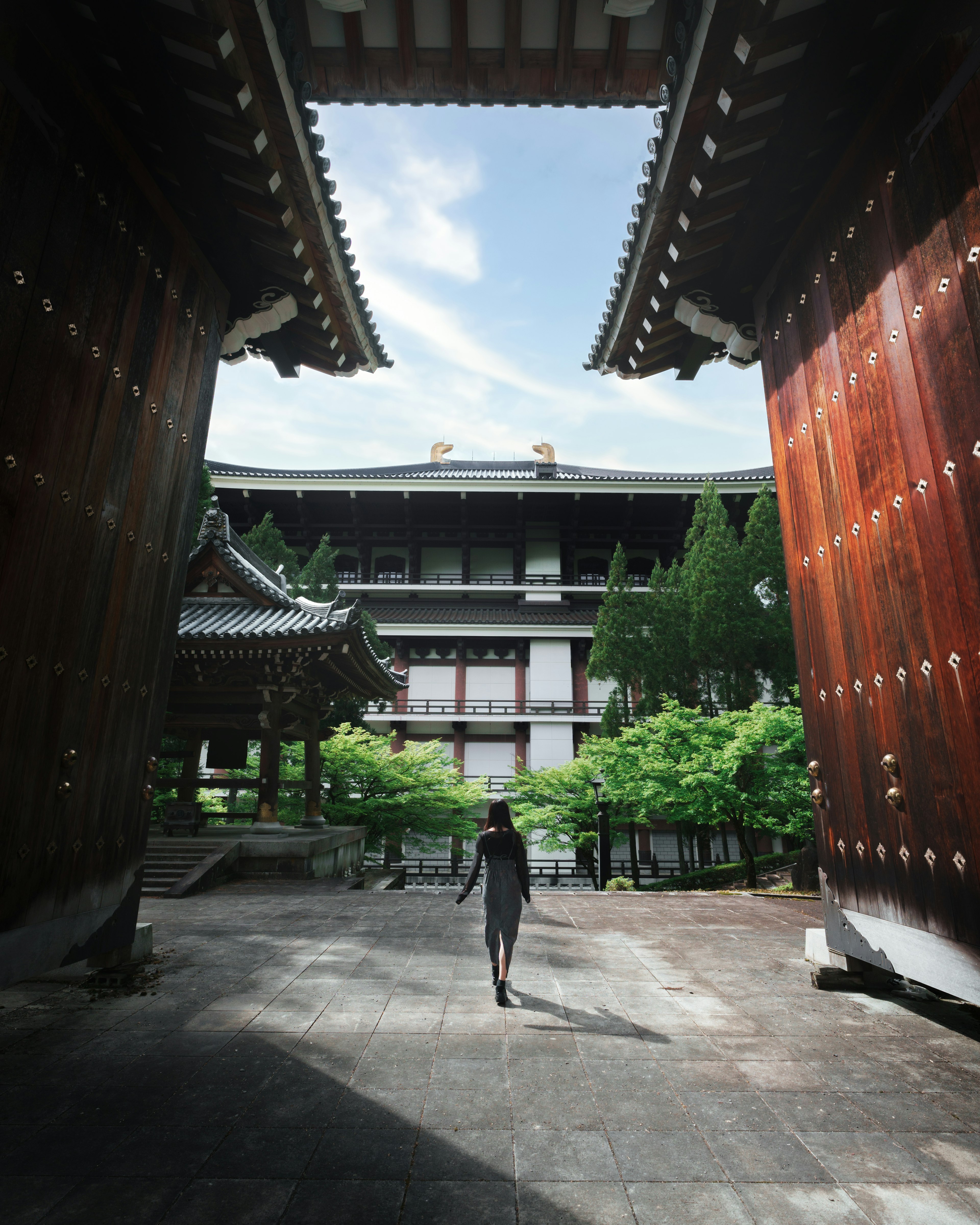 Person walking through large wooden gates with greenery in the background