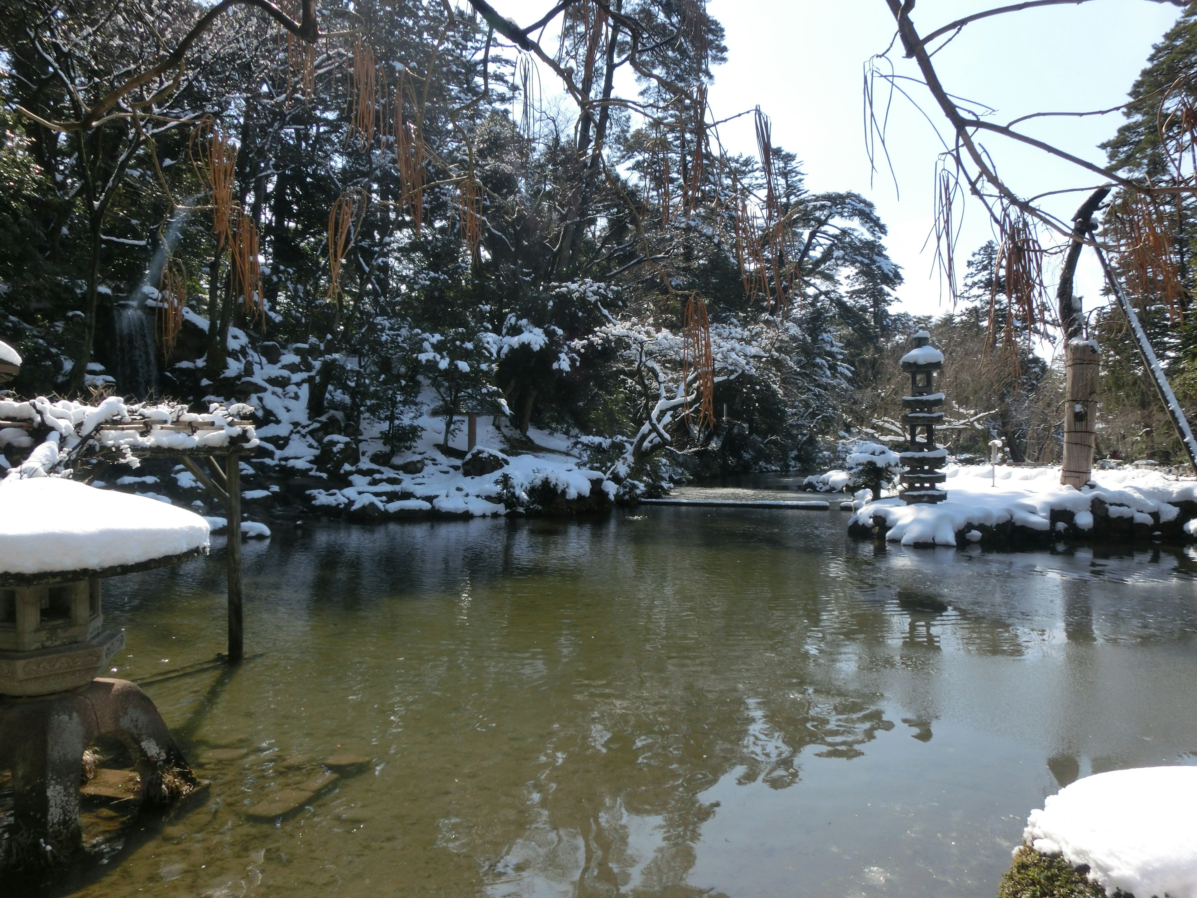 Estanque de jardín cubierto de nieve con linterna de piedra y árboles