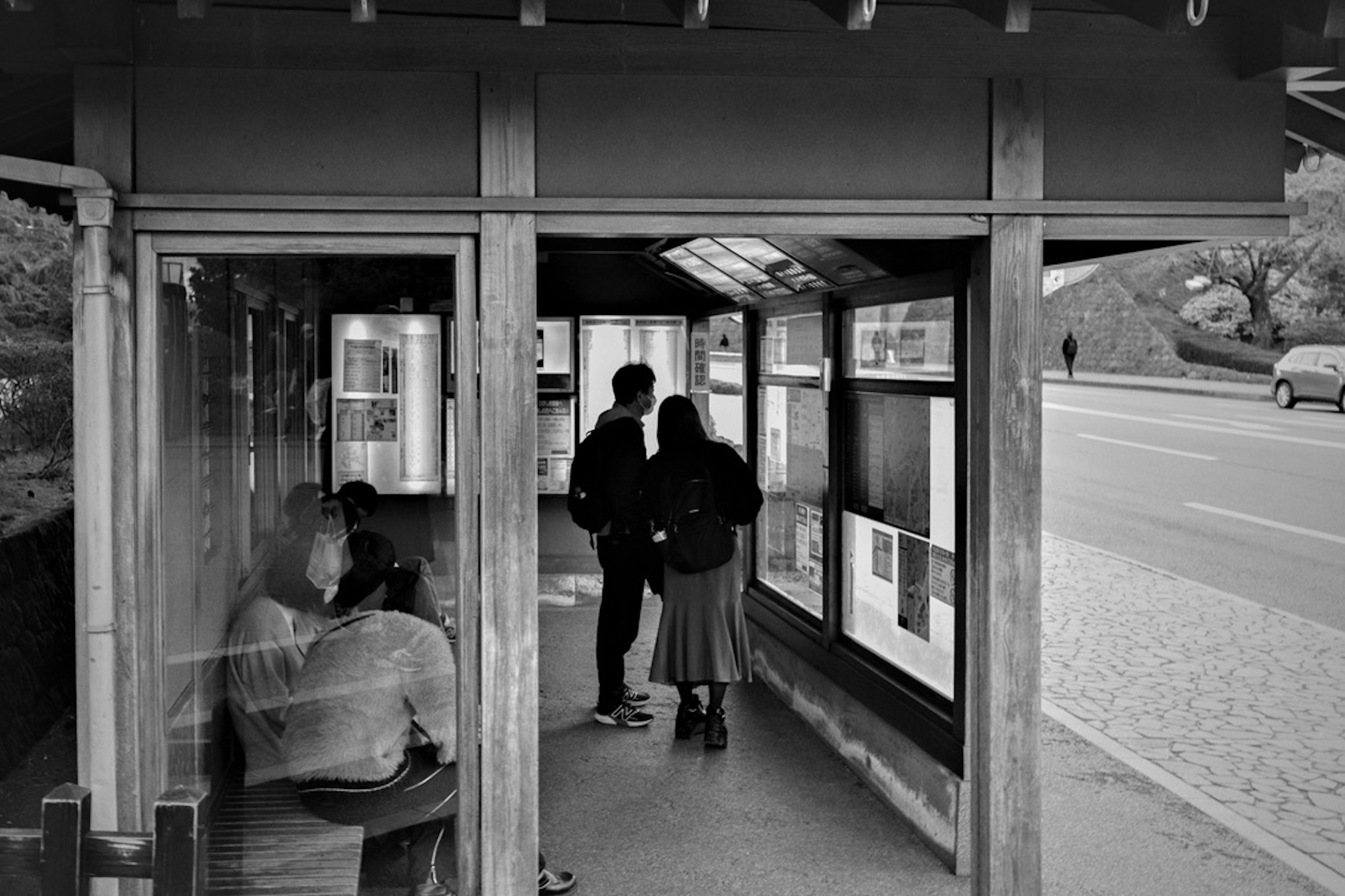 Black and white photo of a couple talking at a bus stop with a seated person